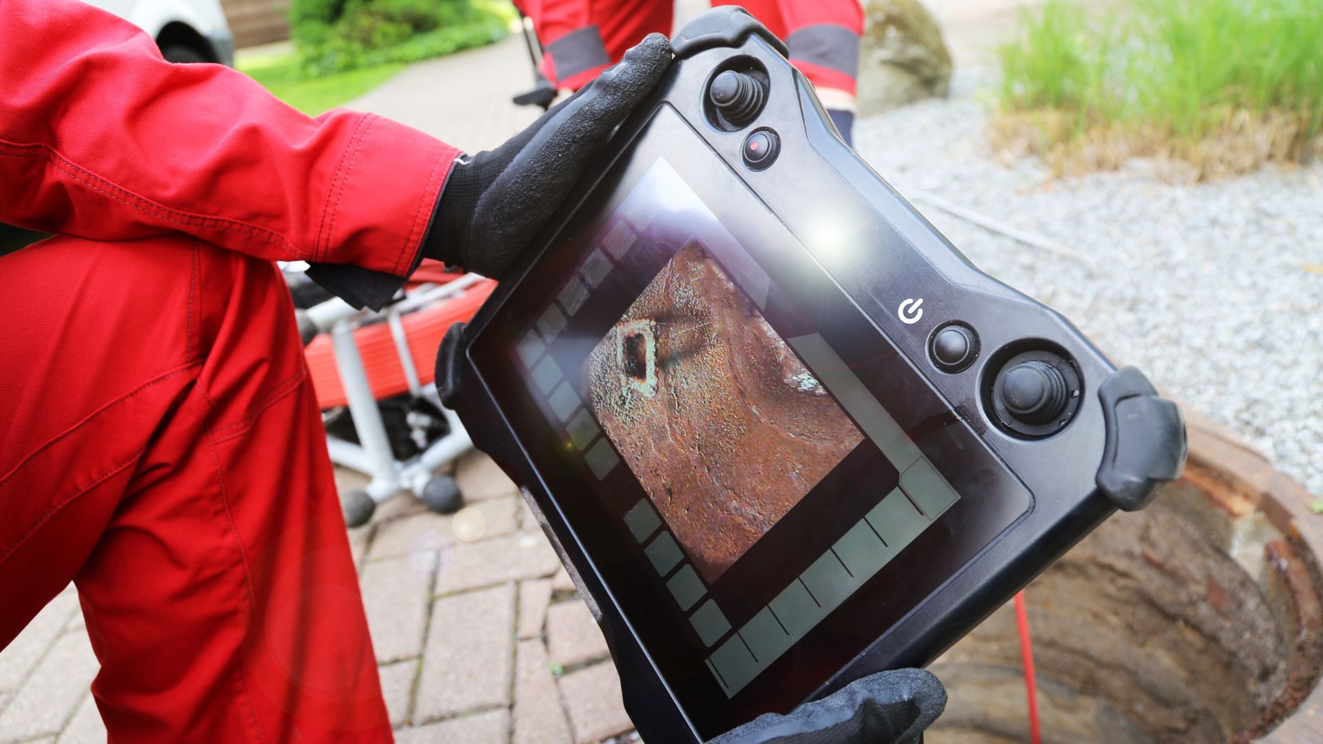 Person in red coveralls holding a tablet displaying an inspection of a brown, cylindrical structure.