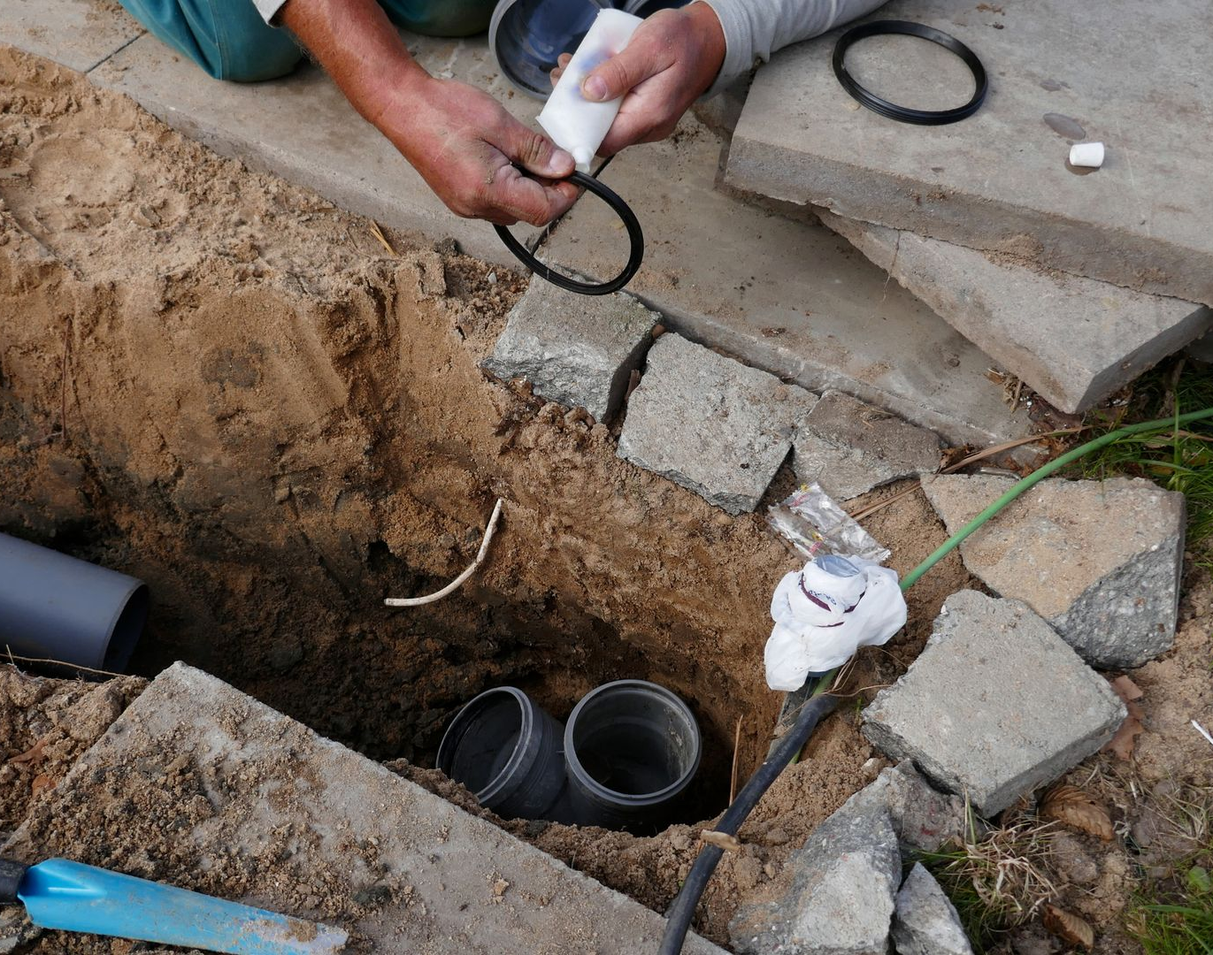 Person installing a black rubber ring in an excavated area with plumbing pipes.