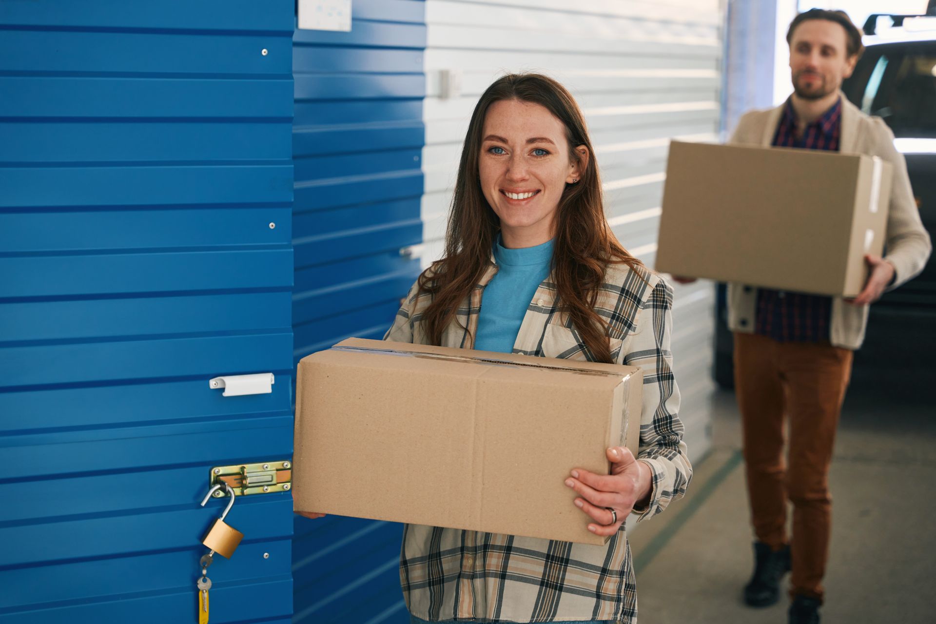 Two people carrying cardboard boxes inside a storage facility.