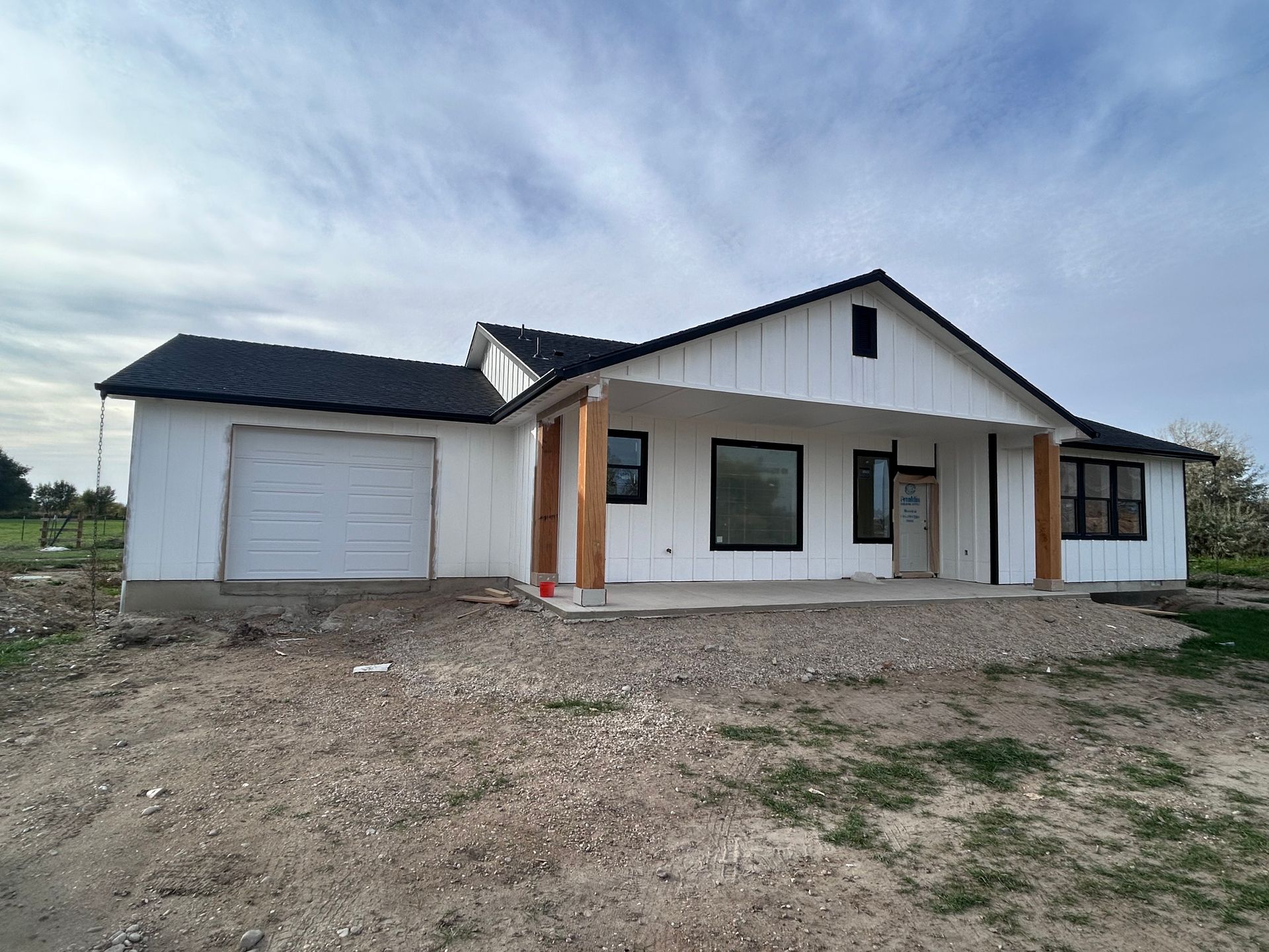 A white house with a black roof is sitting on top of a dirt field.