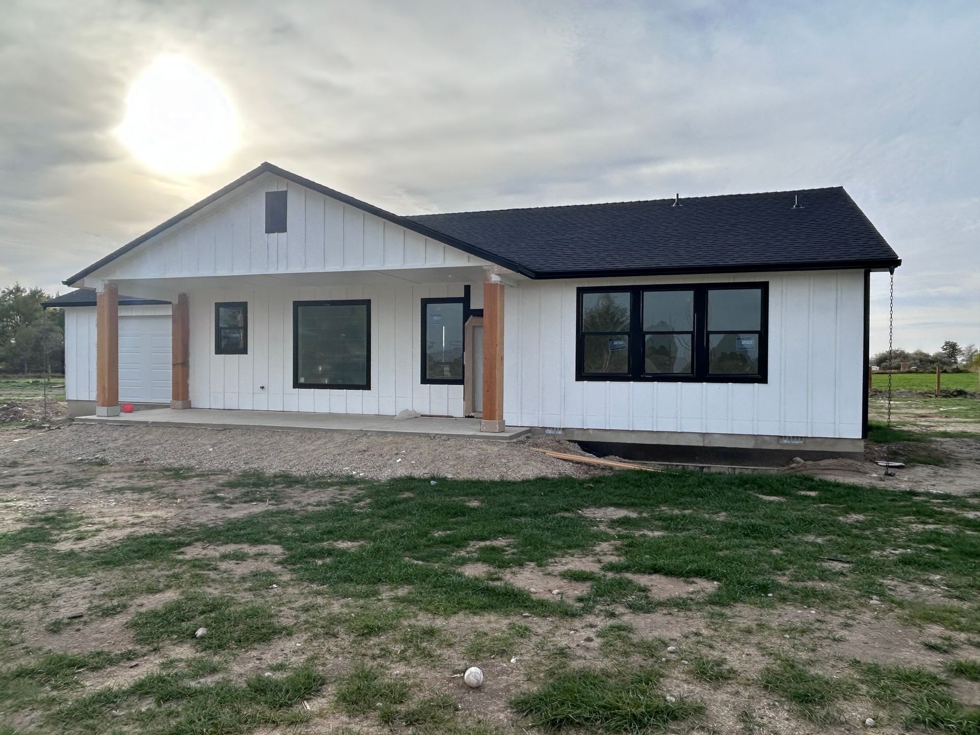 A white house with black windows is sitting in the middle of a grassy field.