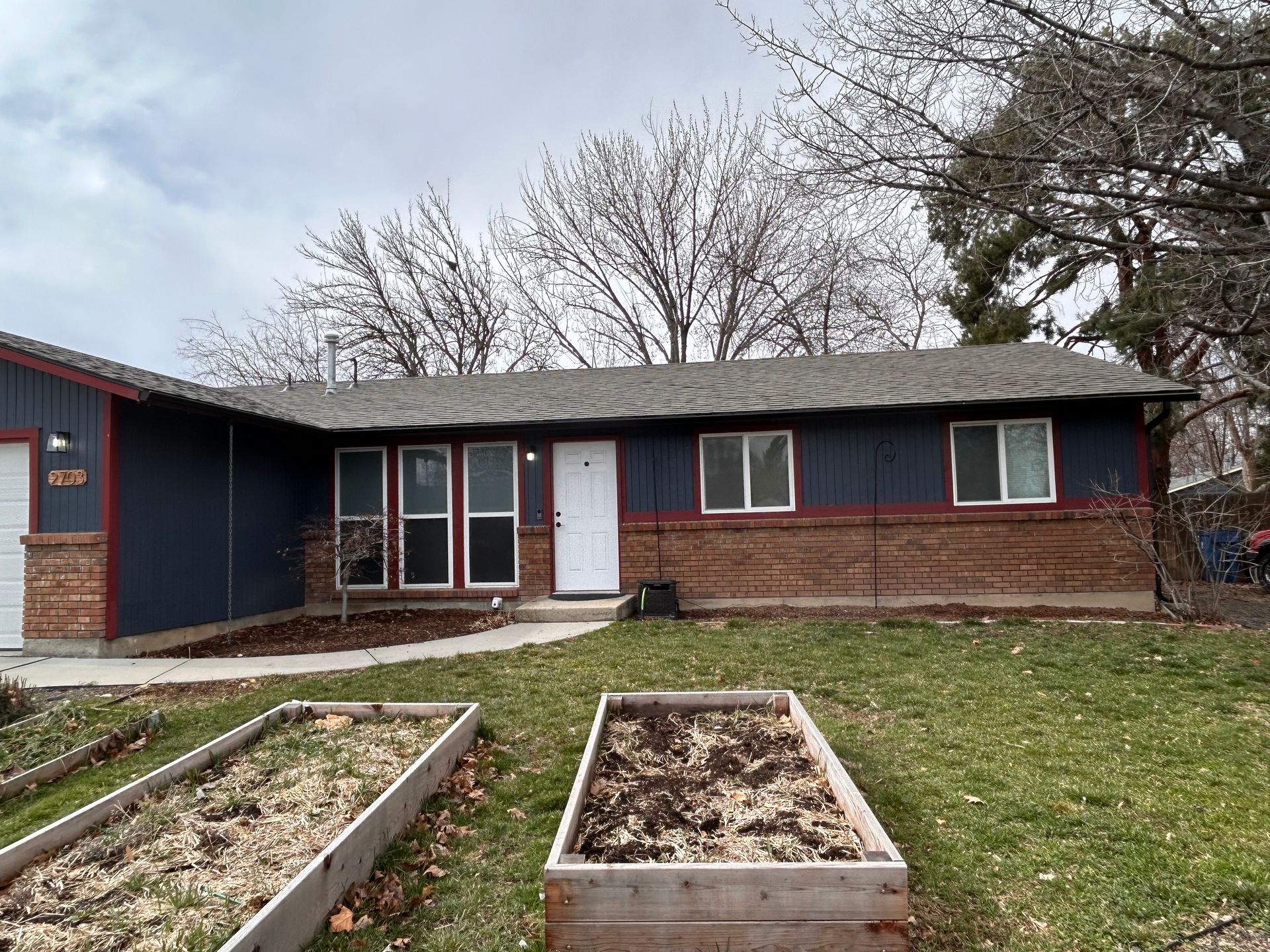 A blue house with a brick roof and a garden in front of it.