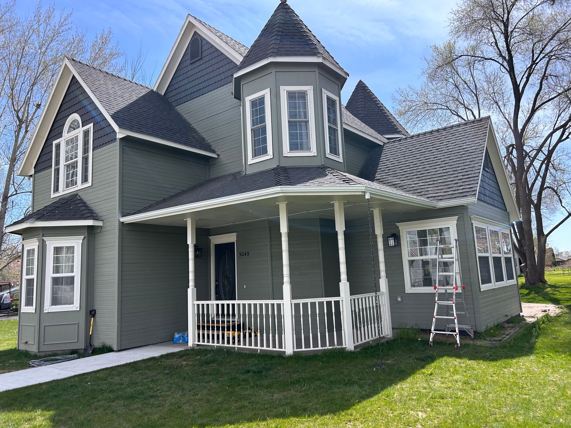 A large house with a porch and a ladder in front of it.