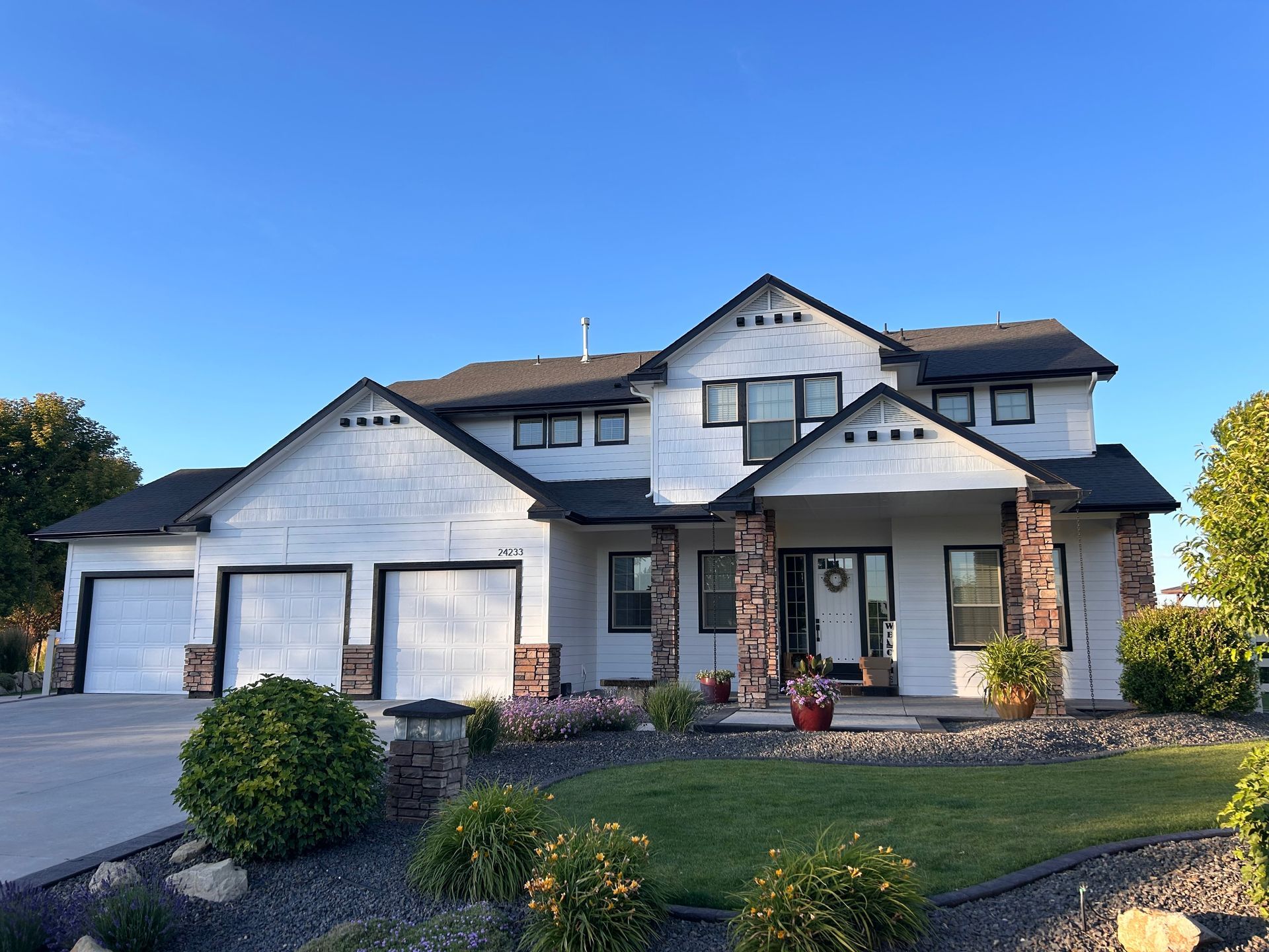 A large white house with a black roof is sitting on top of a lush green lawn.