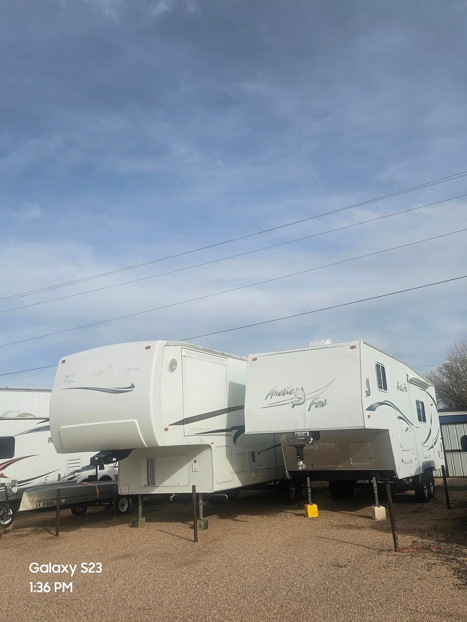 White RVs parked on gravel under a cloudy sky.