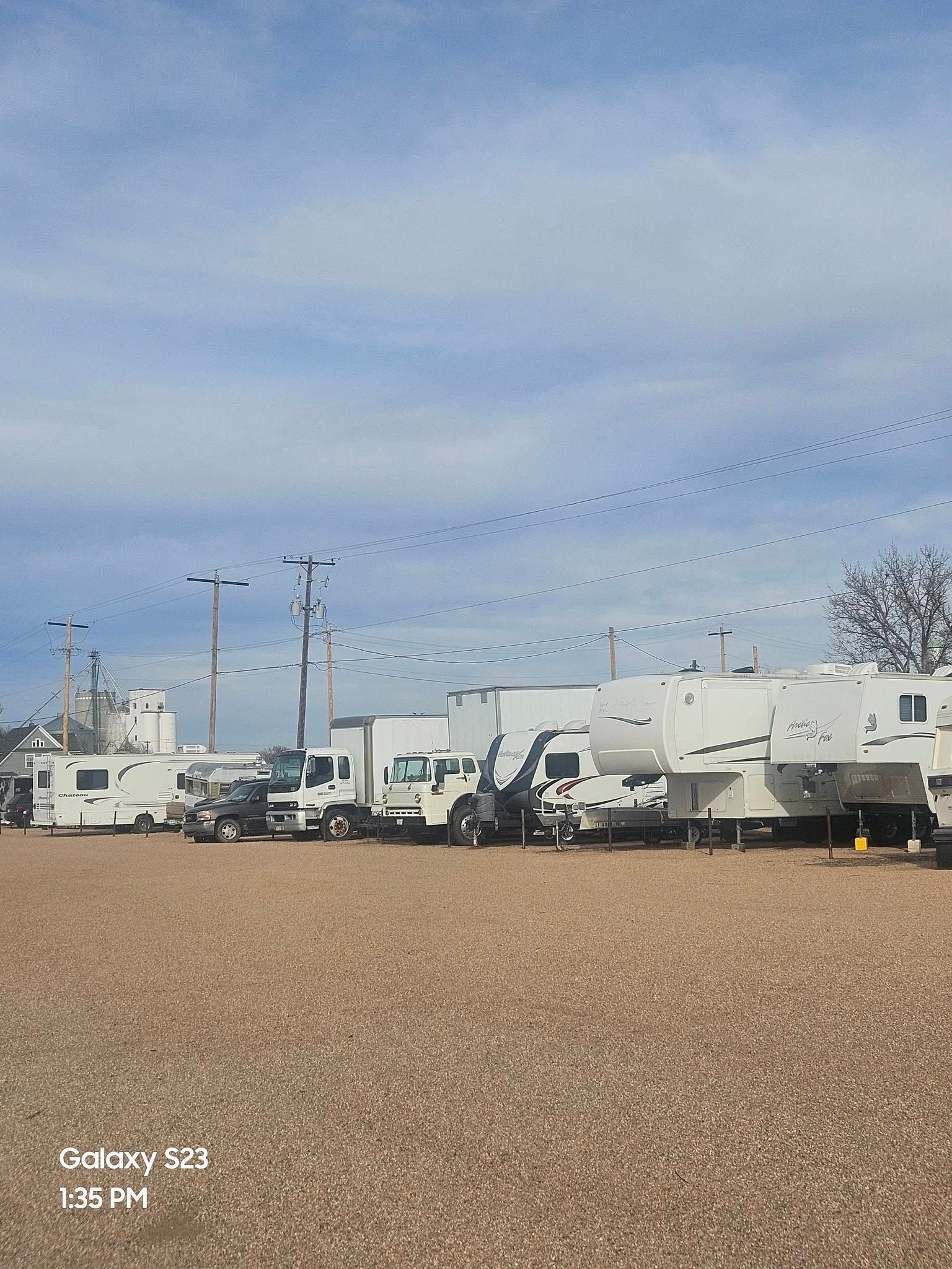 White trucks and RVs parked on a gravel lot under a cloudy blue sky.