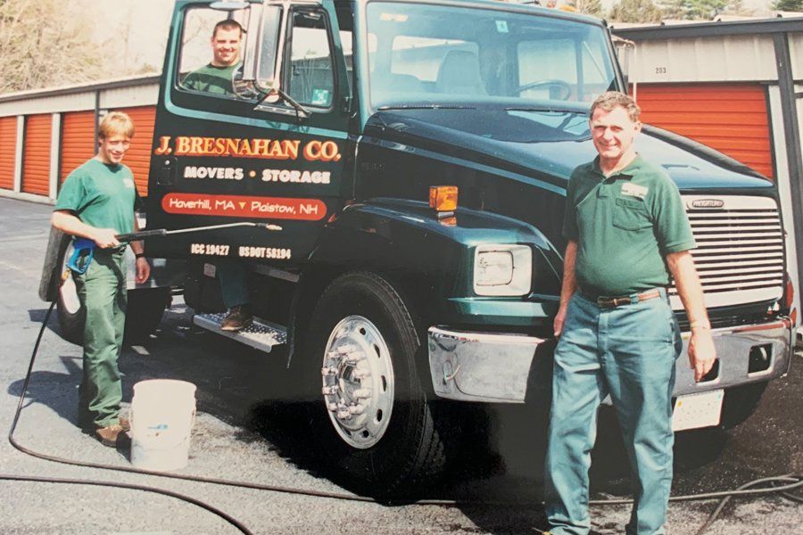 Image of a black truck with company logo sitting in front of storage units.  There are three men in the photo that are working on cleaning the truck.