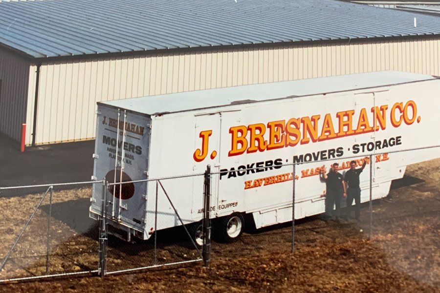 Image of a large white truck with company logo on it.  There are two men standing in front of the truck waving.