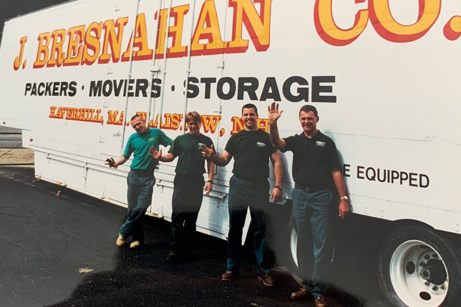 Image of a large white truck with company logo.  There are four men in the photo that are leaning on the truck and waving.