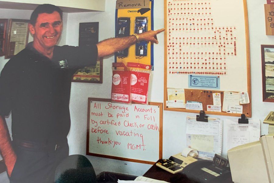 Image of a man standing in office with one hand in pocket and the other pointing to a busy white board on the wall.