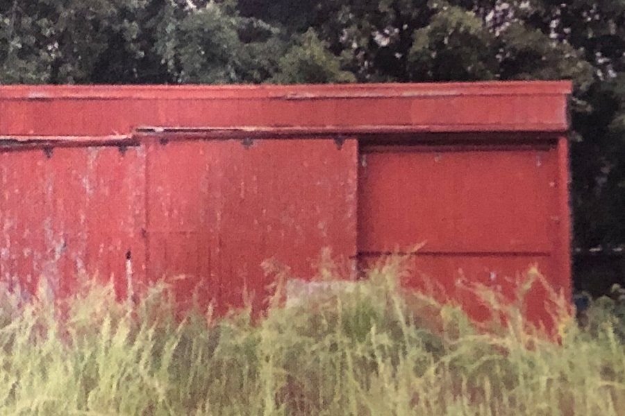 Image of a red horse barn shown in a hay field with lots of trees in the background.