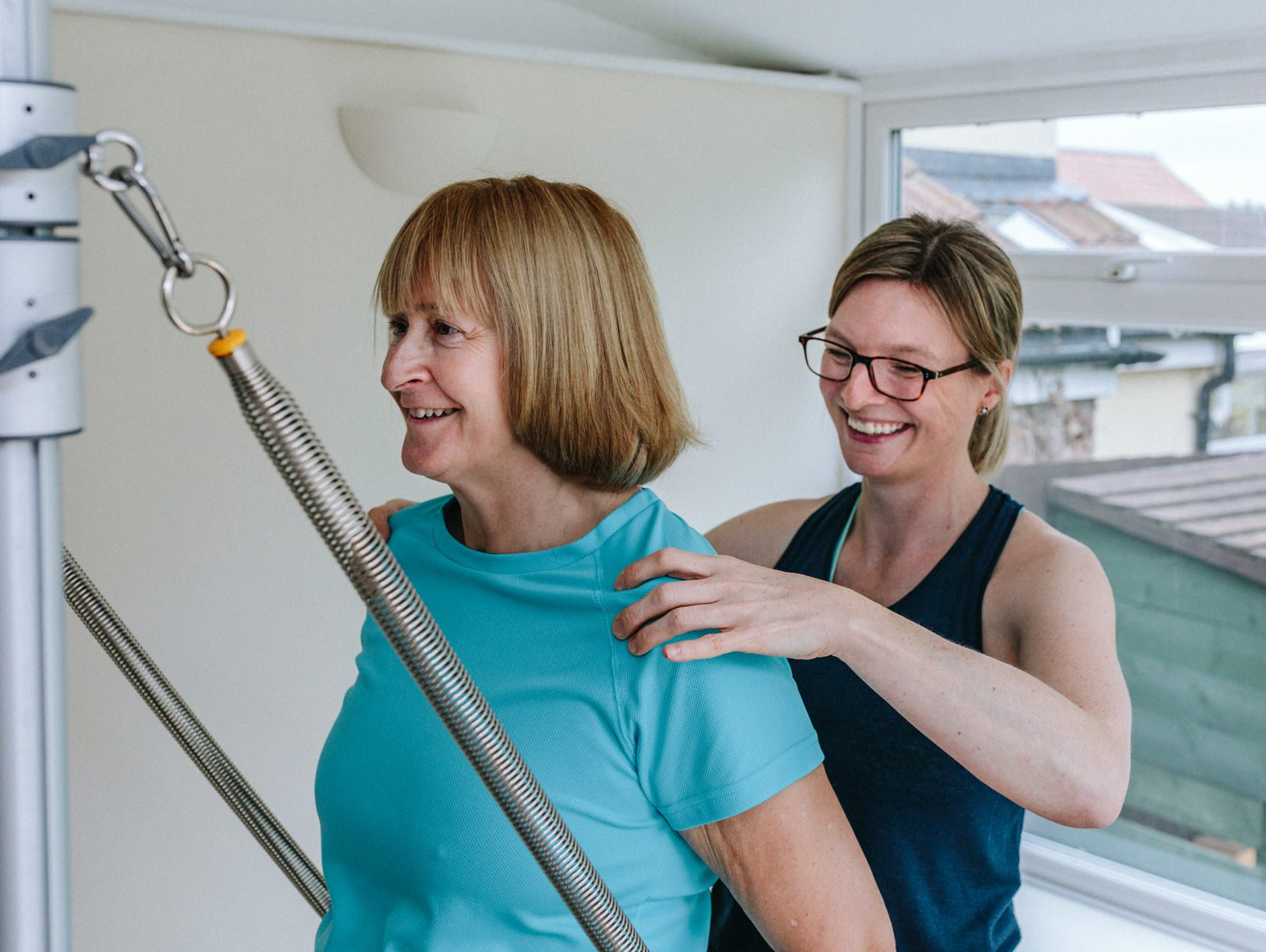 A woman is helping another woman do exercises on a machine.