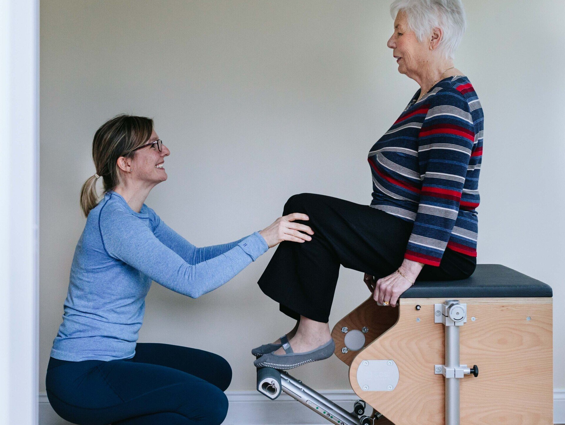 A woman is helping an older woman do exercises on a pilates machine.