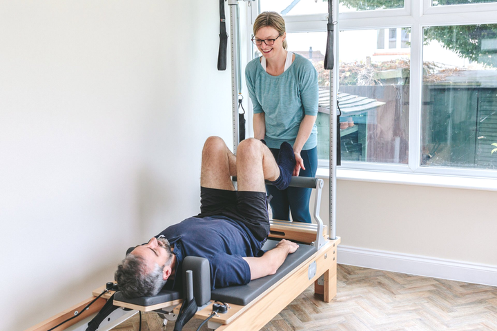 A woman is helping a man do exercises on a pilates machine.