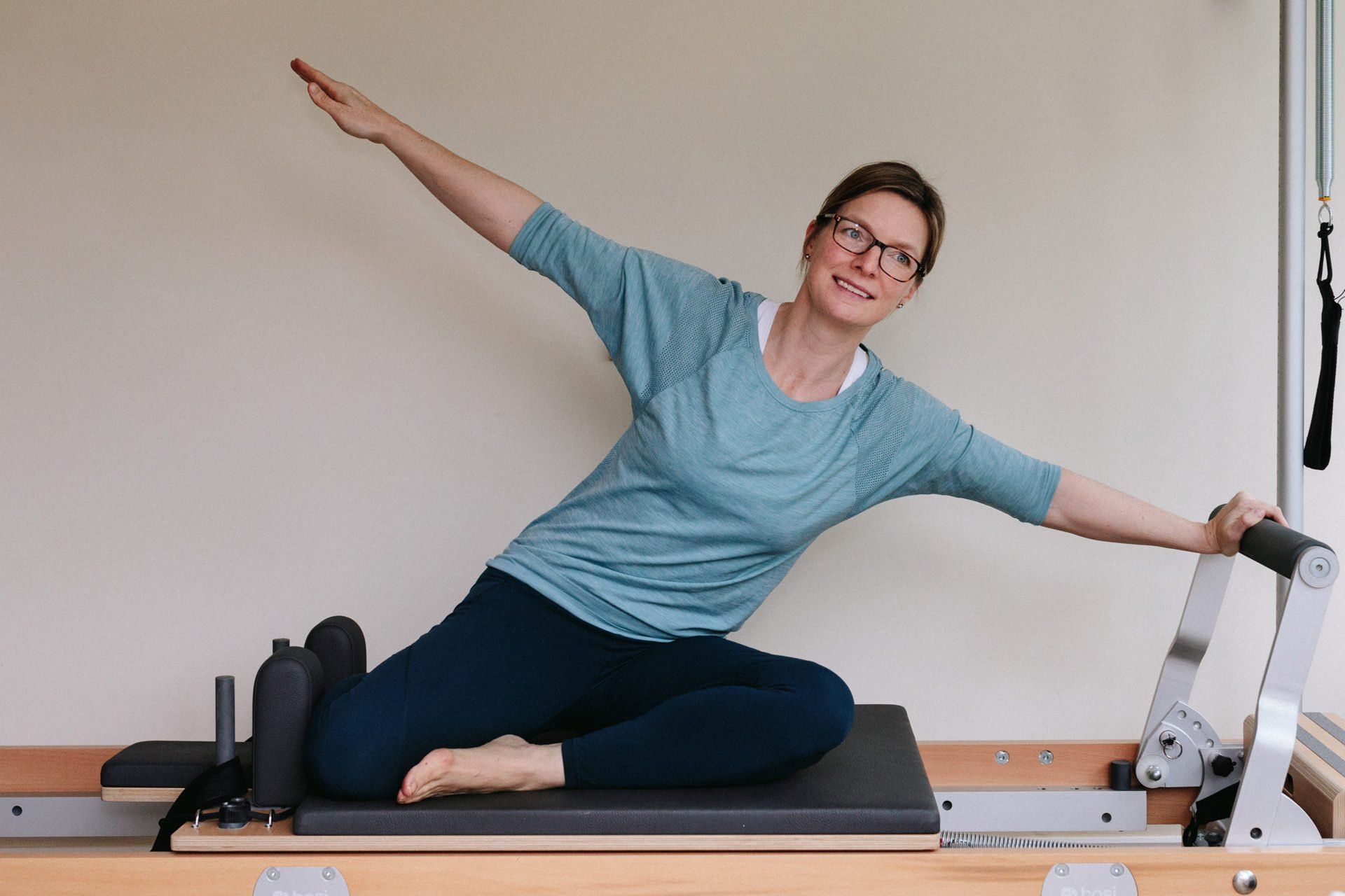 A woman is sitting on a pilates machine with her arms outstretched.