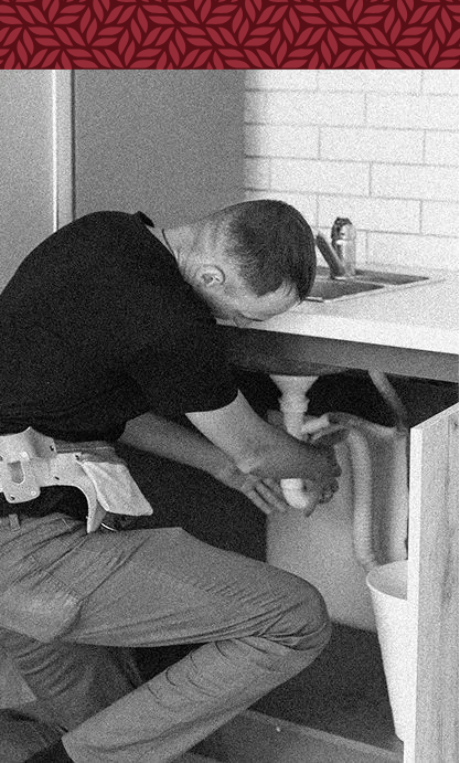 A man is fixing a sink in a black and white photo.