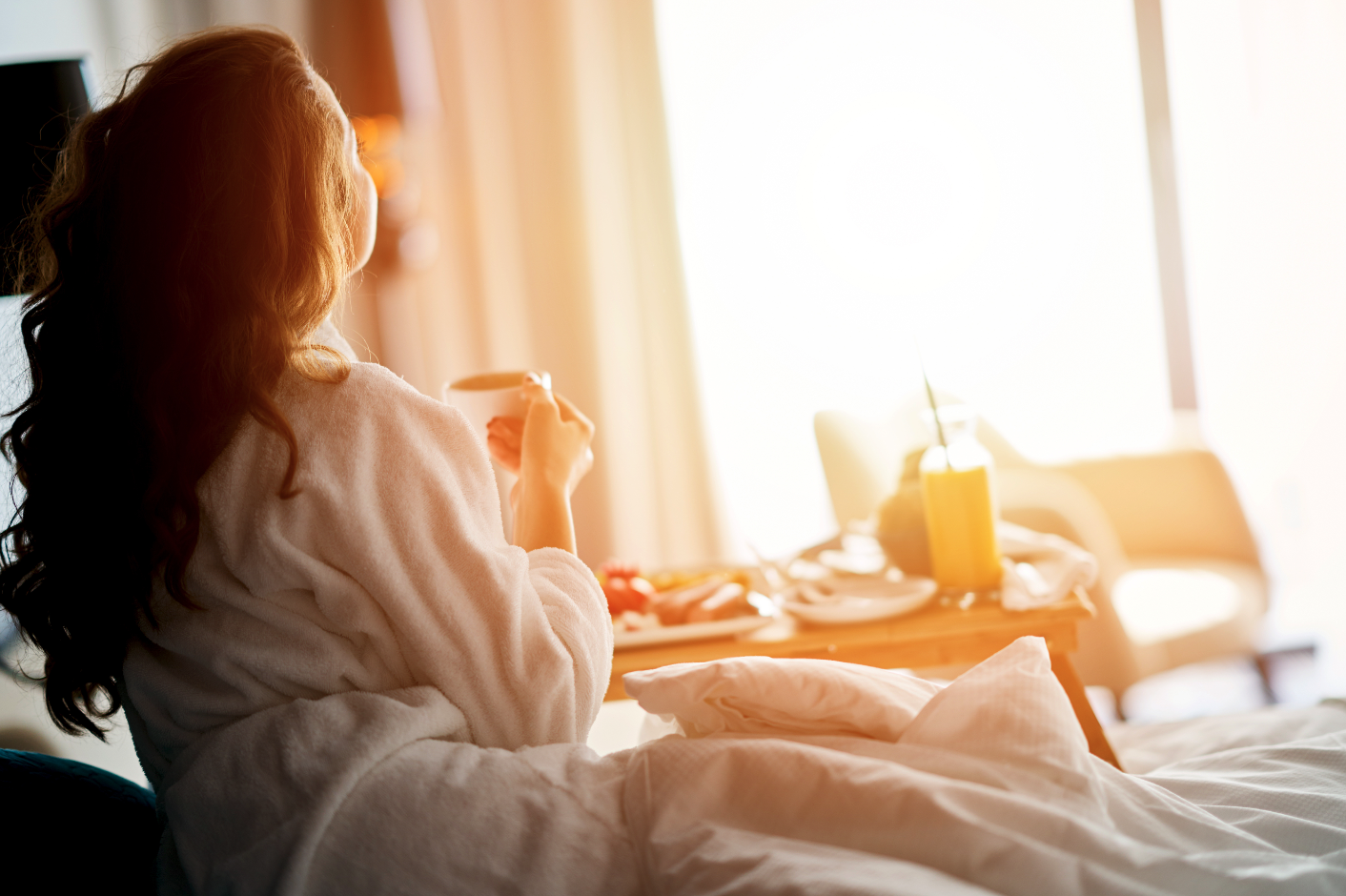 A female hotel guest in a dressing gown enjoying breakfast in bed