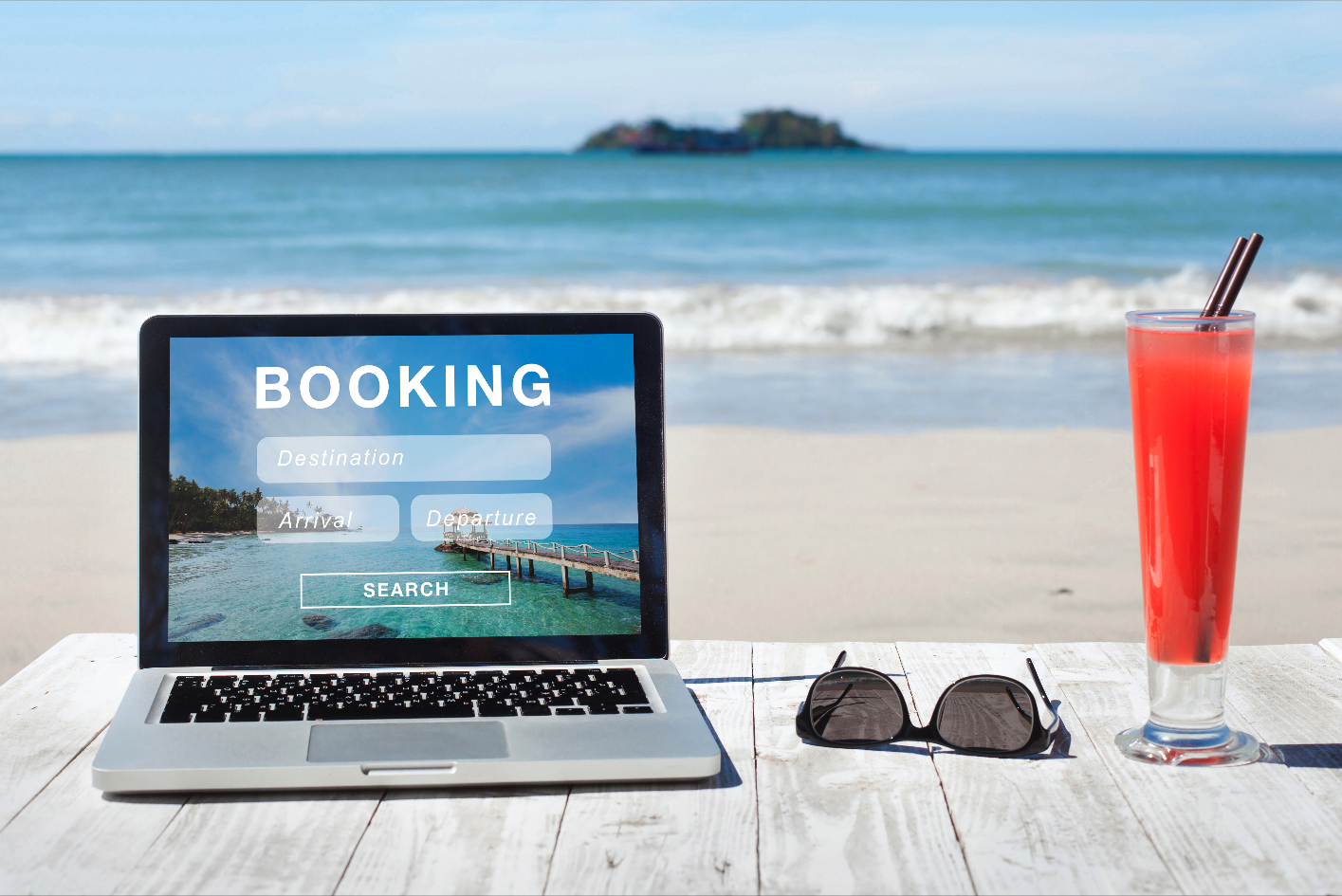 A laptop showing a hotel booking site. A beach is in the background