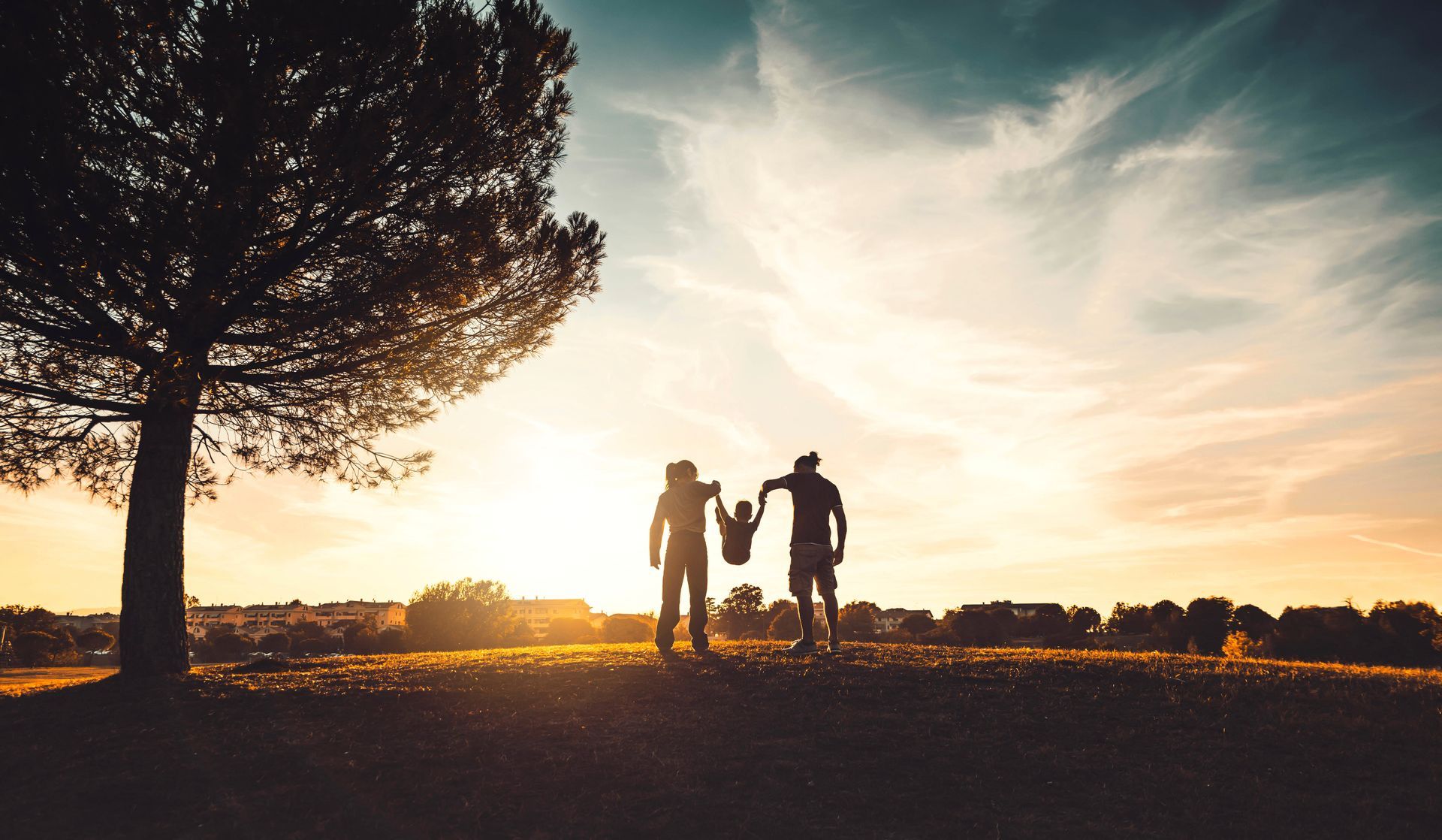 a family standing on top of a hill holding hands at sunset