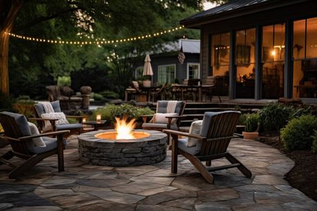 Fire pit with Adirondack chairs on a stone patio, string lights, and a home in the background.