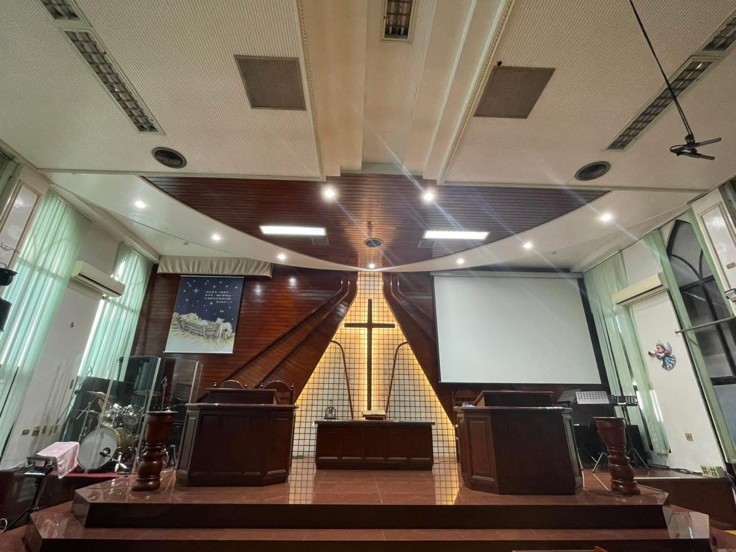 Church interior: wooden altar, cross, pulpit, stage, projection screen, and ceiling lights.