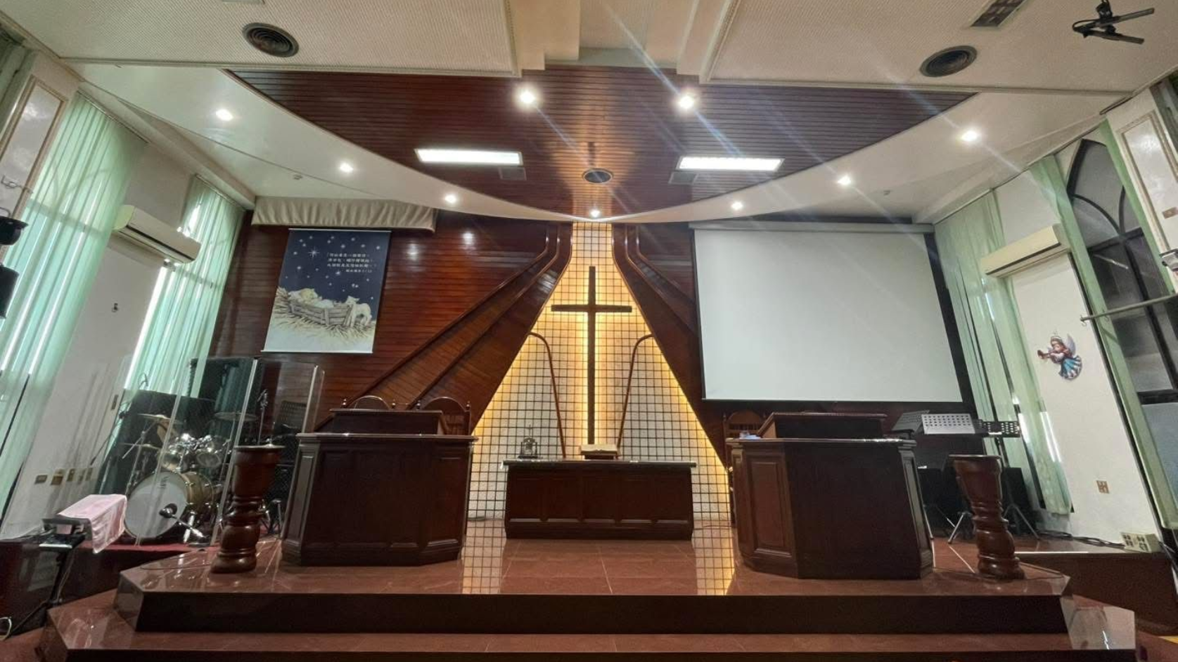 Church interior with altar, cross, lecterns, and stage. Dark wood backdrop, white screen and ceiling, and stage lights.