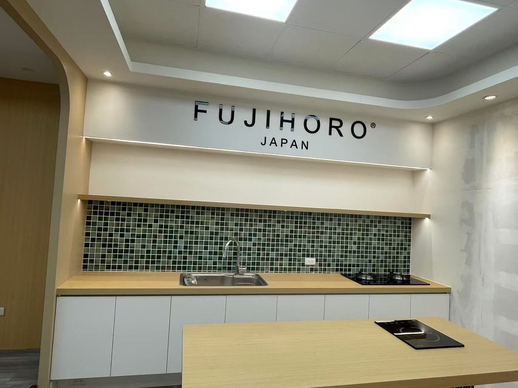 Kitchen display featuring a FUJIHORO Japan logo, white cabinets, wooden countertops, and green tiled backsplash.