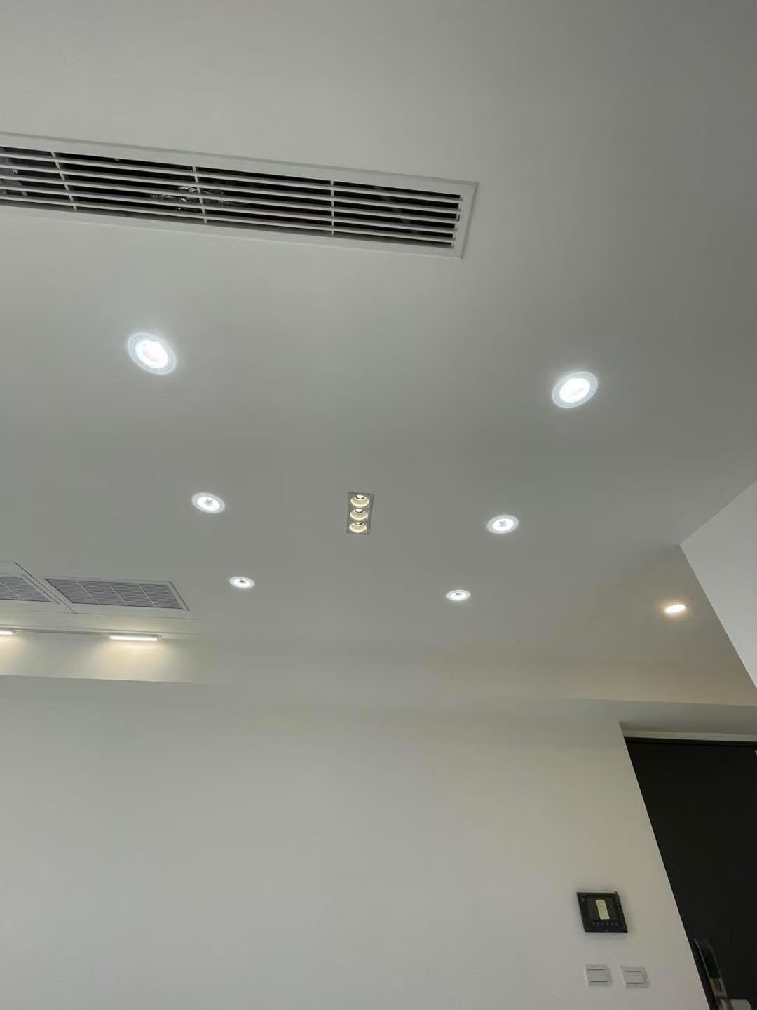 White ceiling with recessed lights, ventilation grates, and a small dark sign.