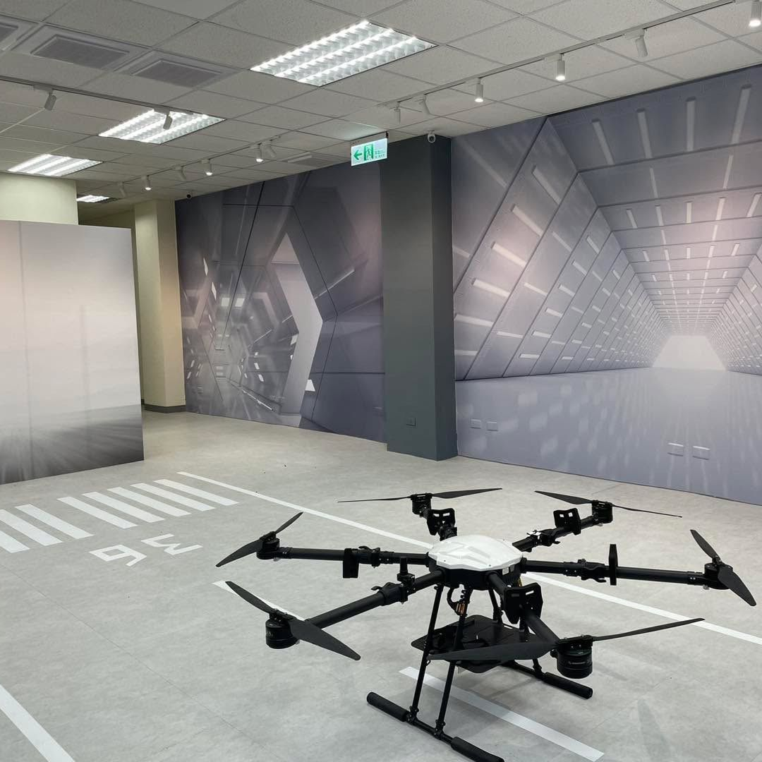 Drone on a grey runway-painted floor, inside a room with futuristic wall art and bright lighting.