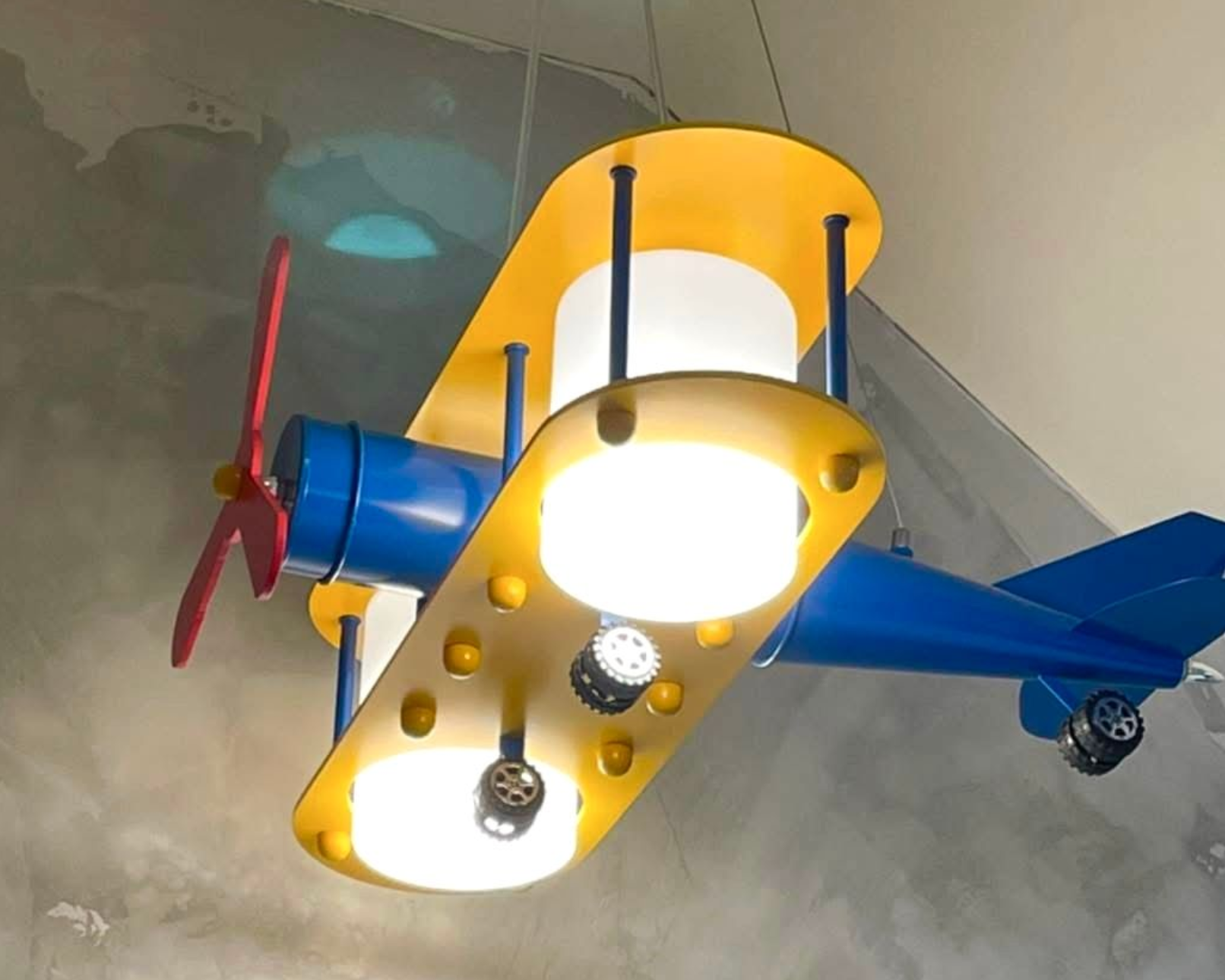 Blue and yellow airplane-shaped ceiling light fixture with red propeller and two glowing lights.