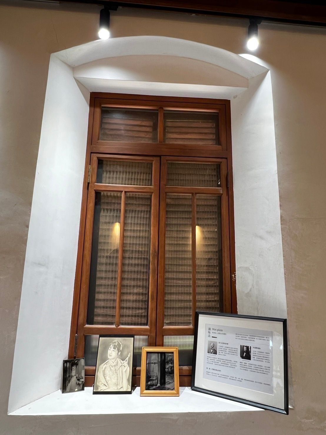 Wooden window in white alcove with photos on the sill, lit by overhead spotlights.