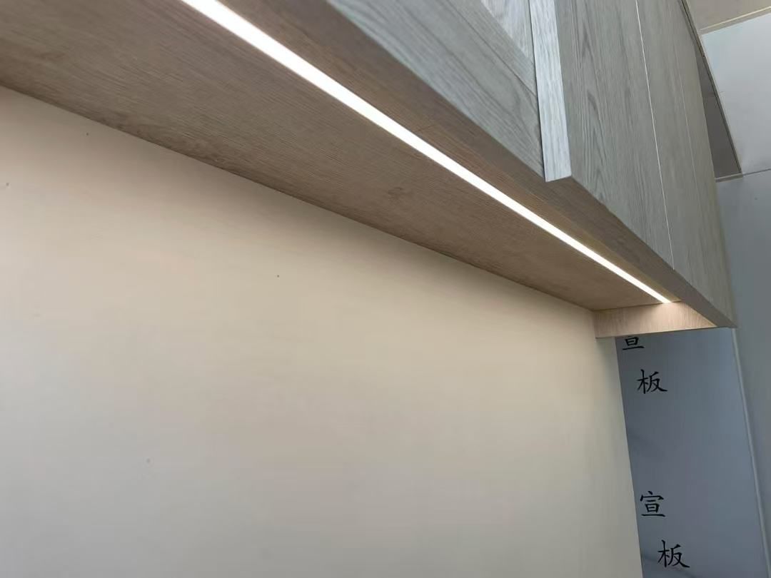 A recessed LED light strip illuminates a wooden shelf over a white wall.