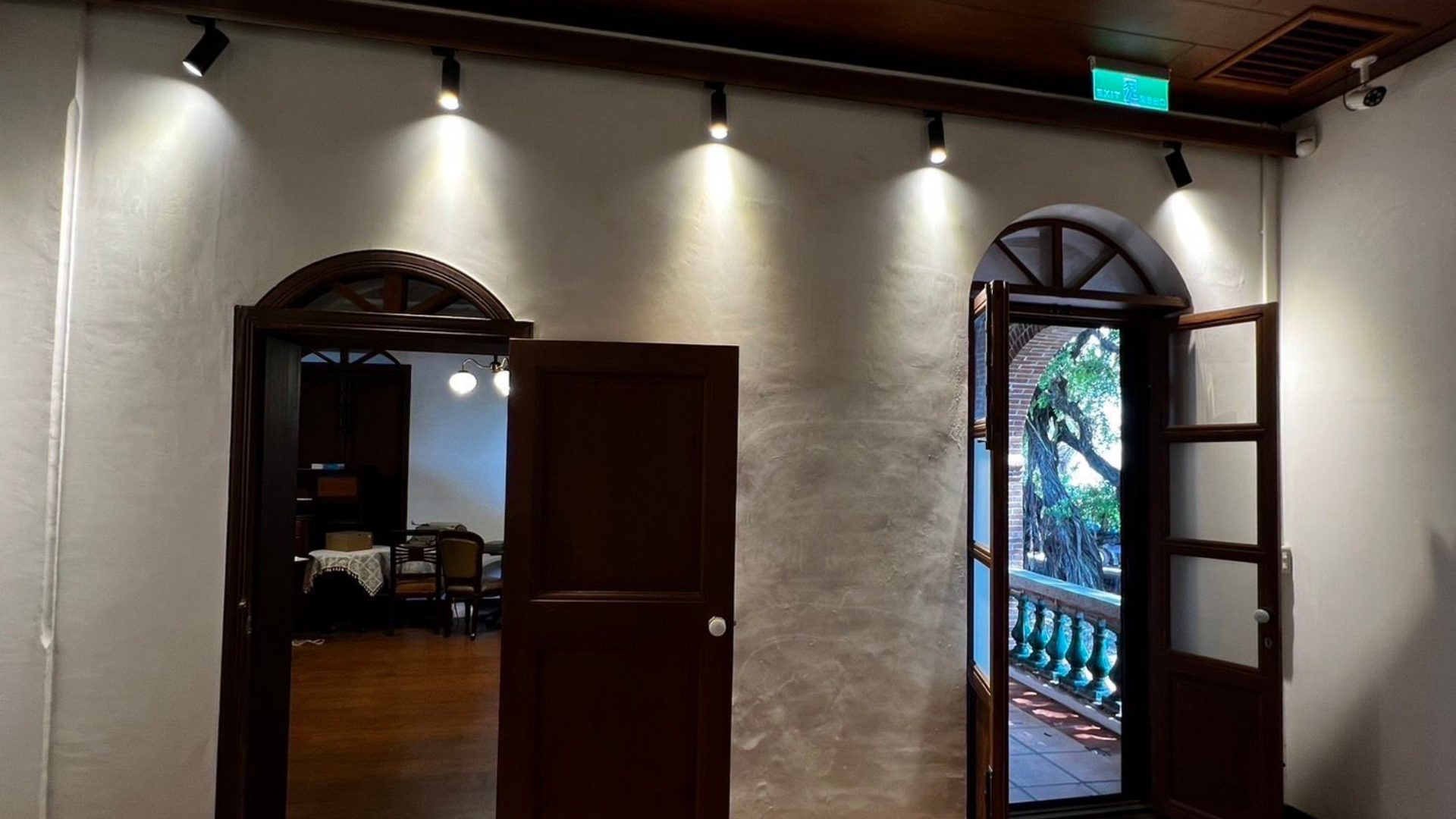 Two dark wooden arched doorways lead to indoor and outdoor spaces, with spotlights overhead.
