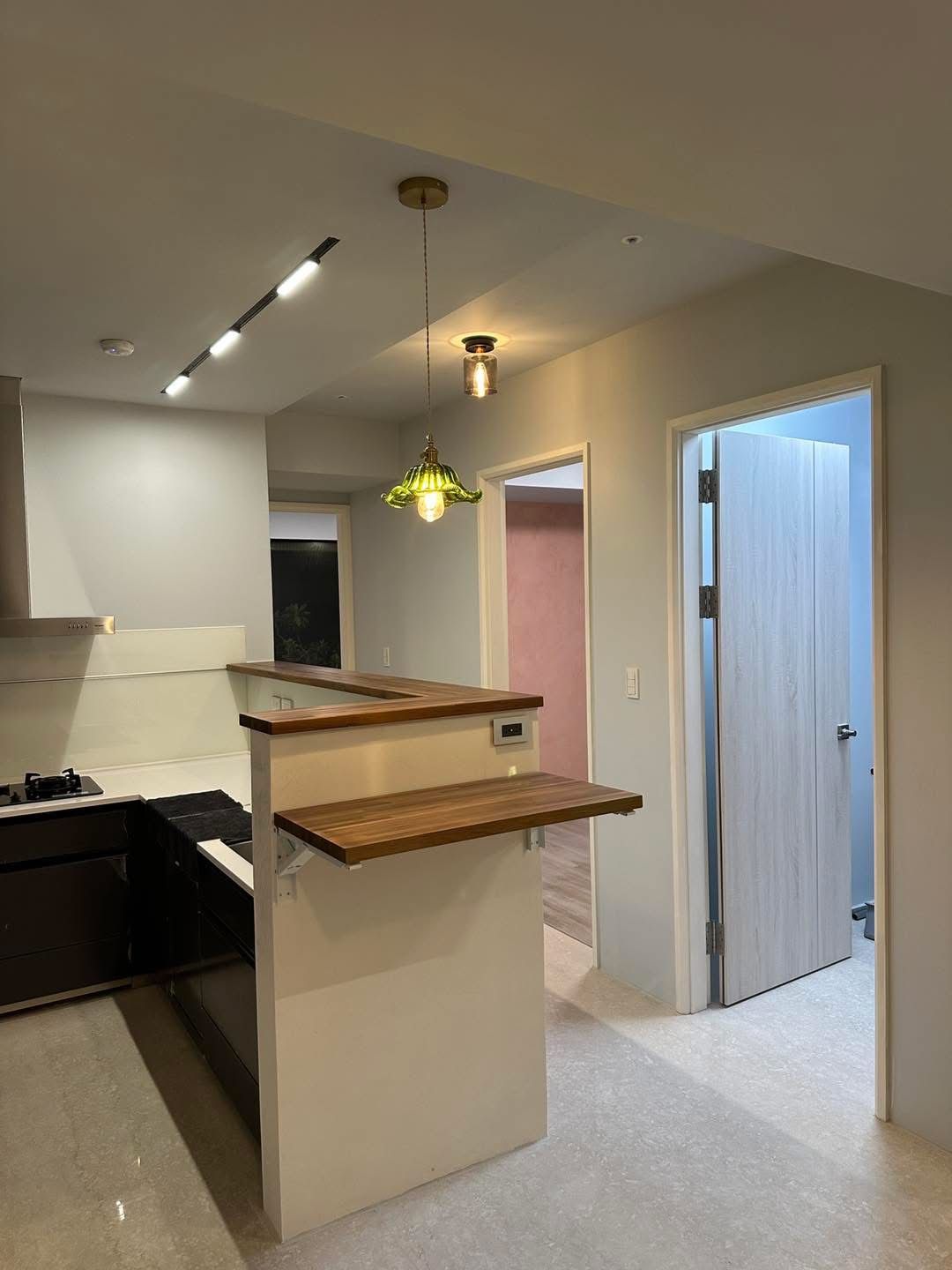 Kitchen with a white island, wooden countertop, and two hanging lights. Doorways lead to other rooms.