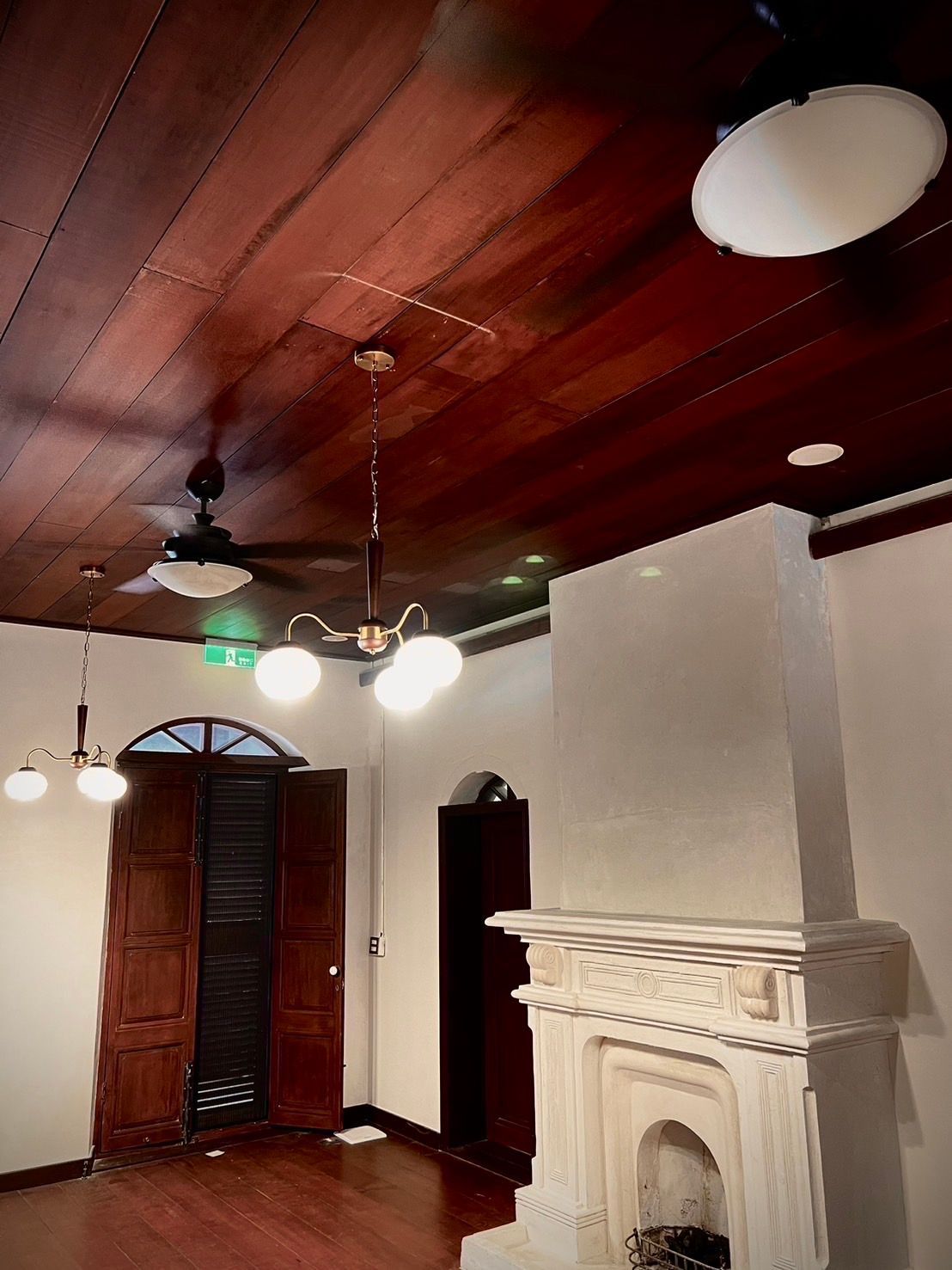 Wooden ceiling with ornate light fixtures, fireplace, and doorway. Room is bathed in warm light.