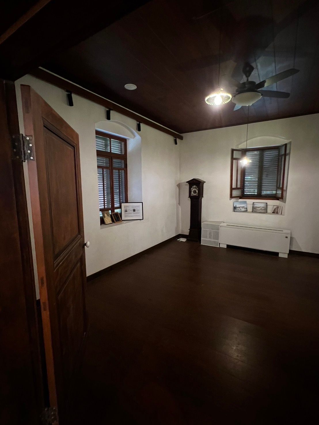 Dark wood-paneled room with windows, an antique clock, and a ceiling fan.