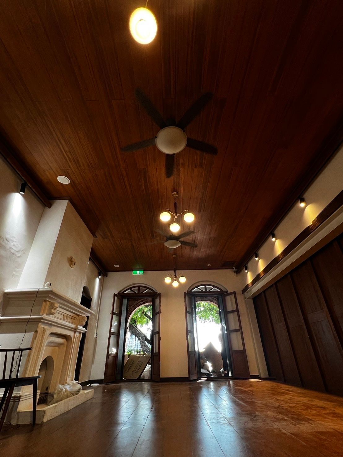 Spacious room with a dark wood ceiling, brown floors, fireplace, and open doorways to the outside.