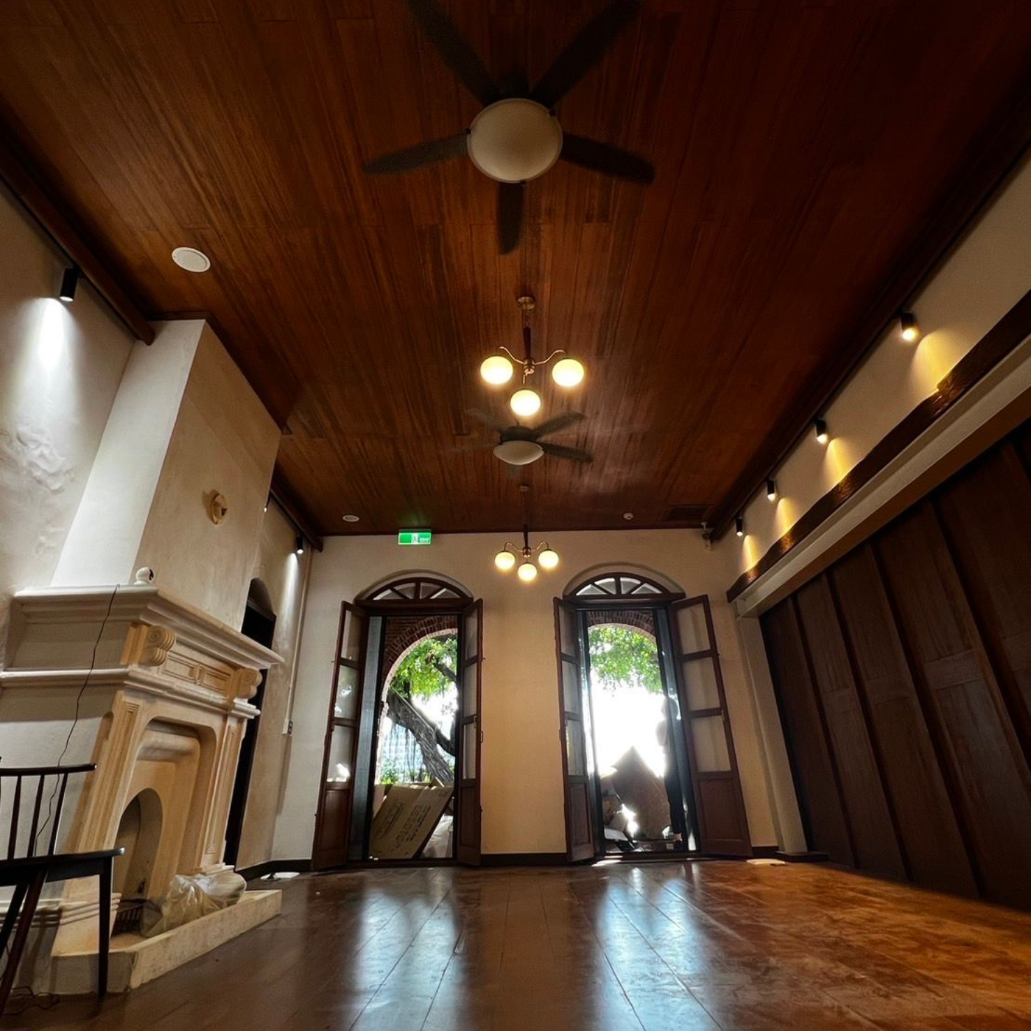 Spacious room with wood ceiling, two open doorways, and a fireplace. Ceiling fans and chandeliers hang above.