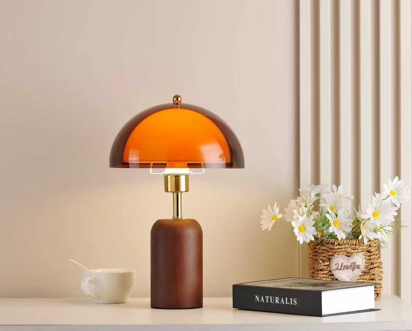 Modern table lamp with orange glass shade, wooden base, and a small flower arrangement on a white table.