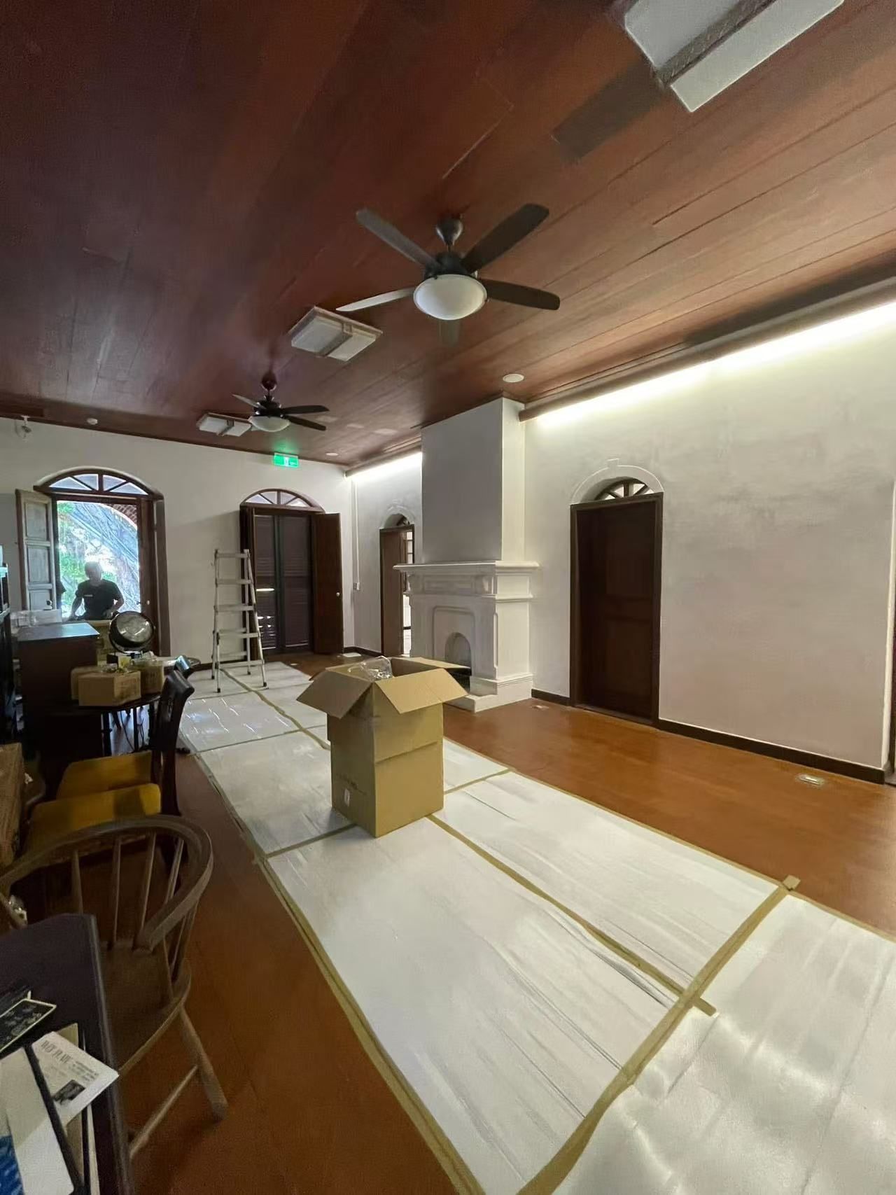 Interior with wood ceiling, floors, white walls. Boxes and protective covering on the floor. Doors and fireplace.