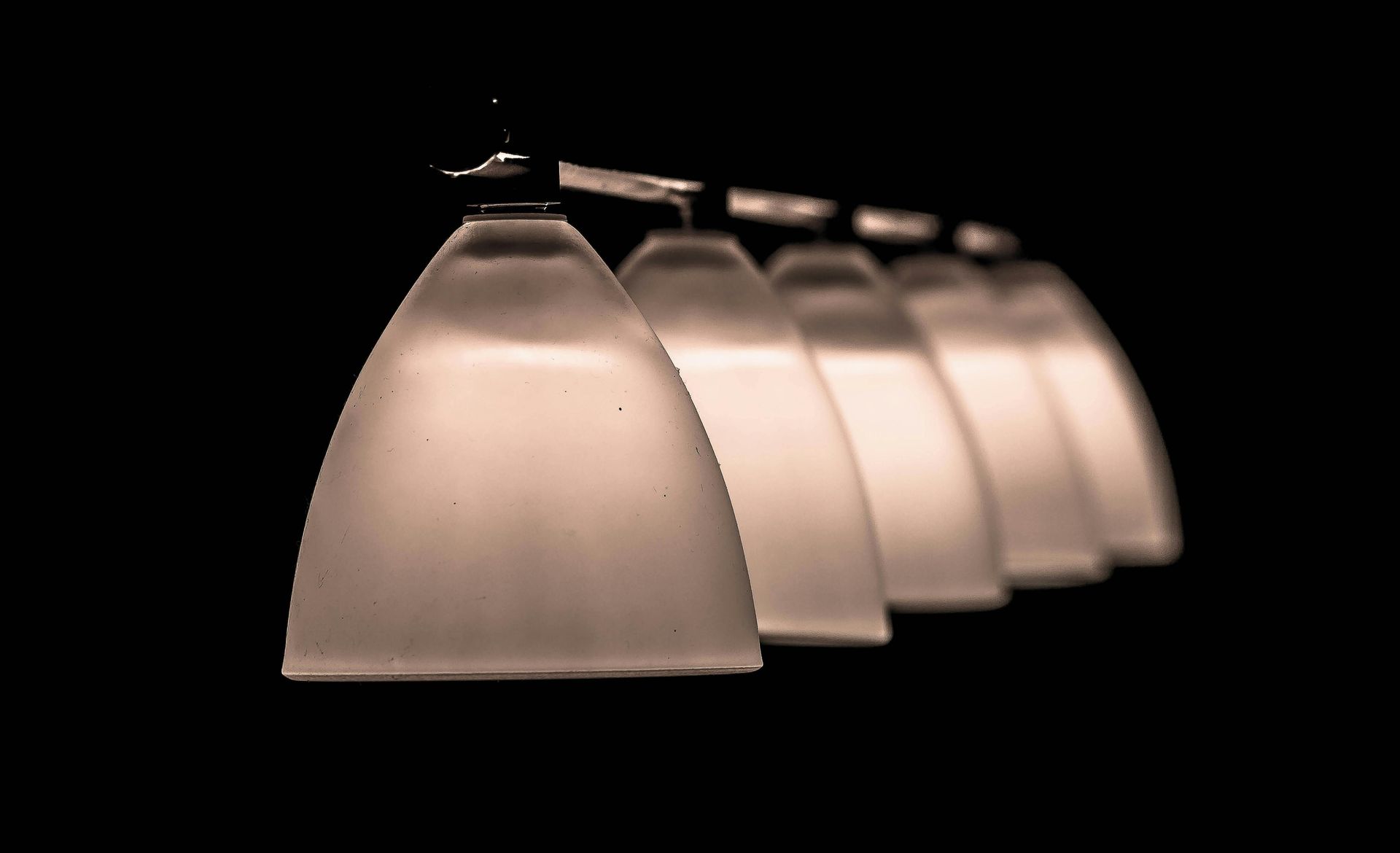 Row of frosted glass lamps hanging against a black background.