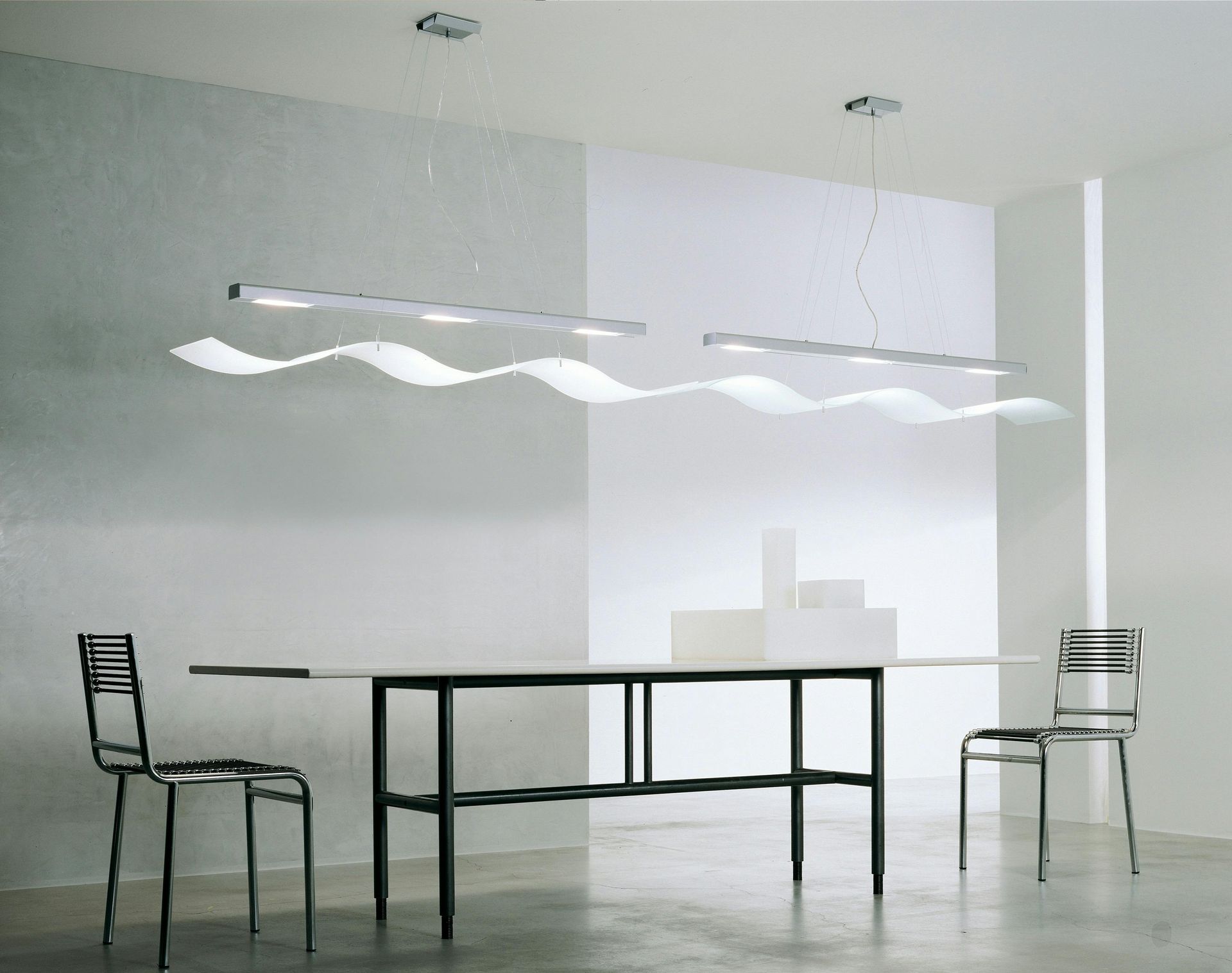 Modern dining room with a long table, minimalist chairs, and wave-shaped ceiling lights.