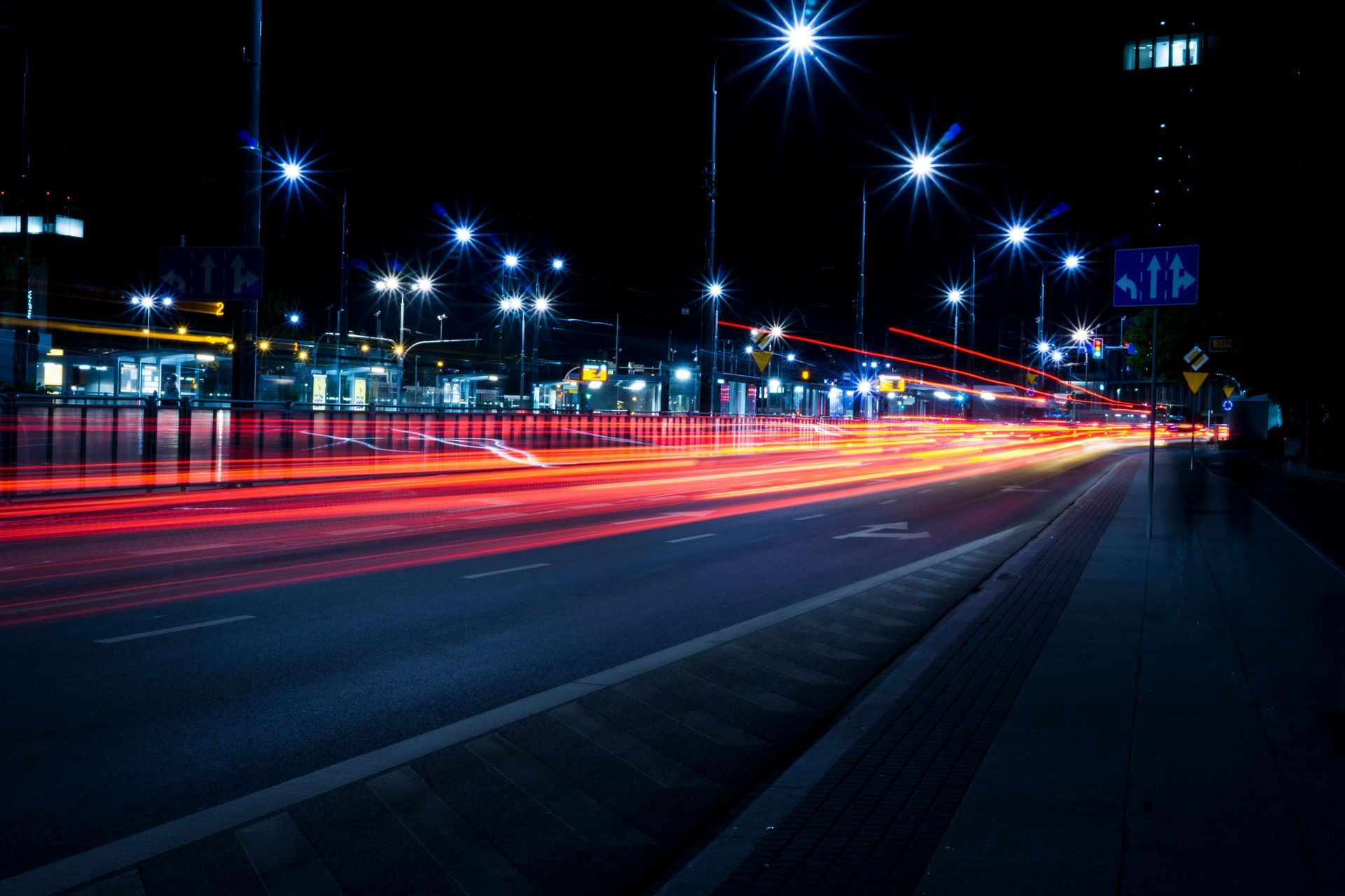 Nighttime city street with blurred red and orange car light trails. Street lights illuminate the road and buildings.