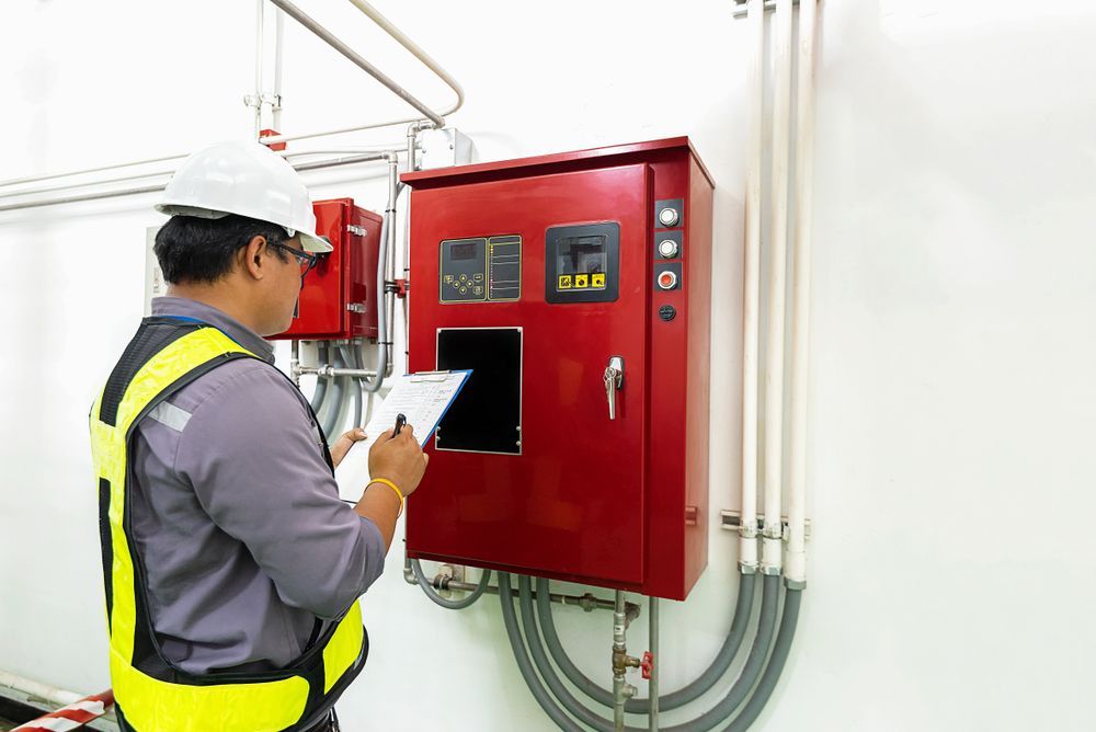 Man in Hard Hat and Vest Inspecting Red Electrical Panel — Fire Maintenance Services (NT) Pty Ltd in Winnellie, NT