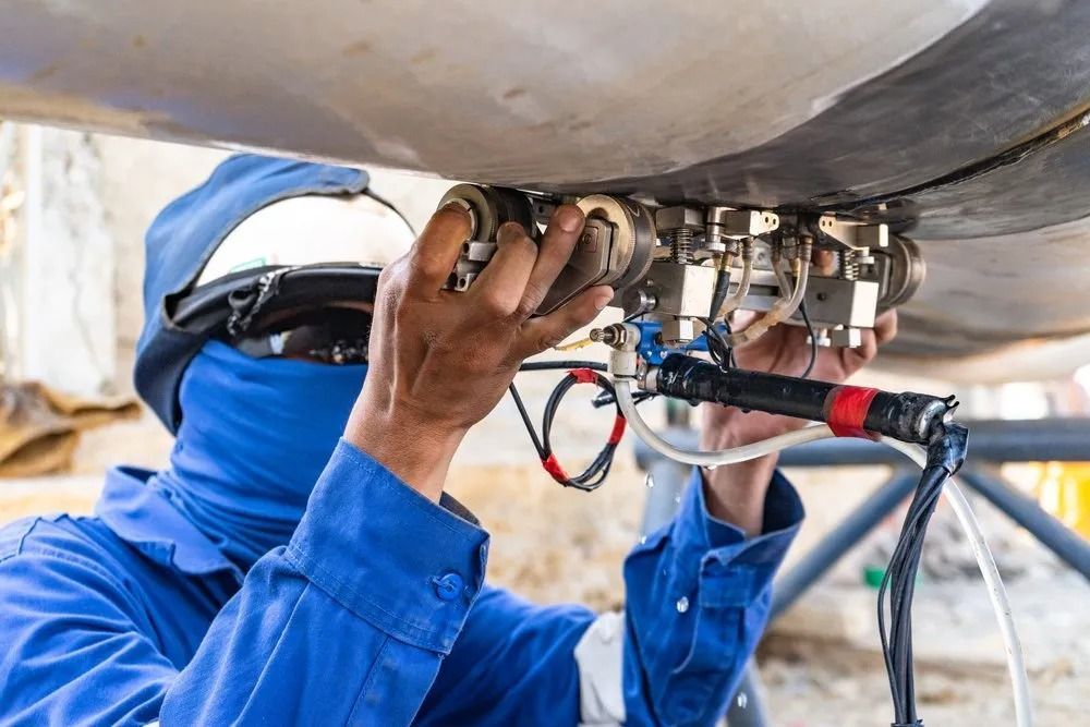 Worker in blue coveralls using inspection equipment on a metal pipe, outdoors. — Fire Maintenance Services (NT) Pty Ltd in Winnellie, NT
