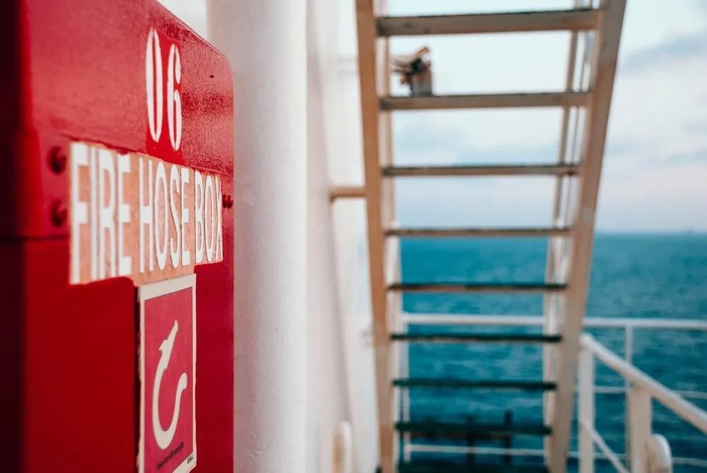 Red fire hose cabinet on a ship deck with a ladder leading to a person against the ocean background. — Fire Maintenance Services (NT) Pty Ltd in Winnellie, NT