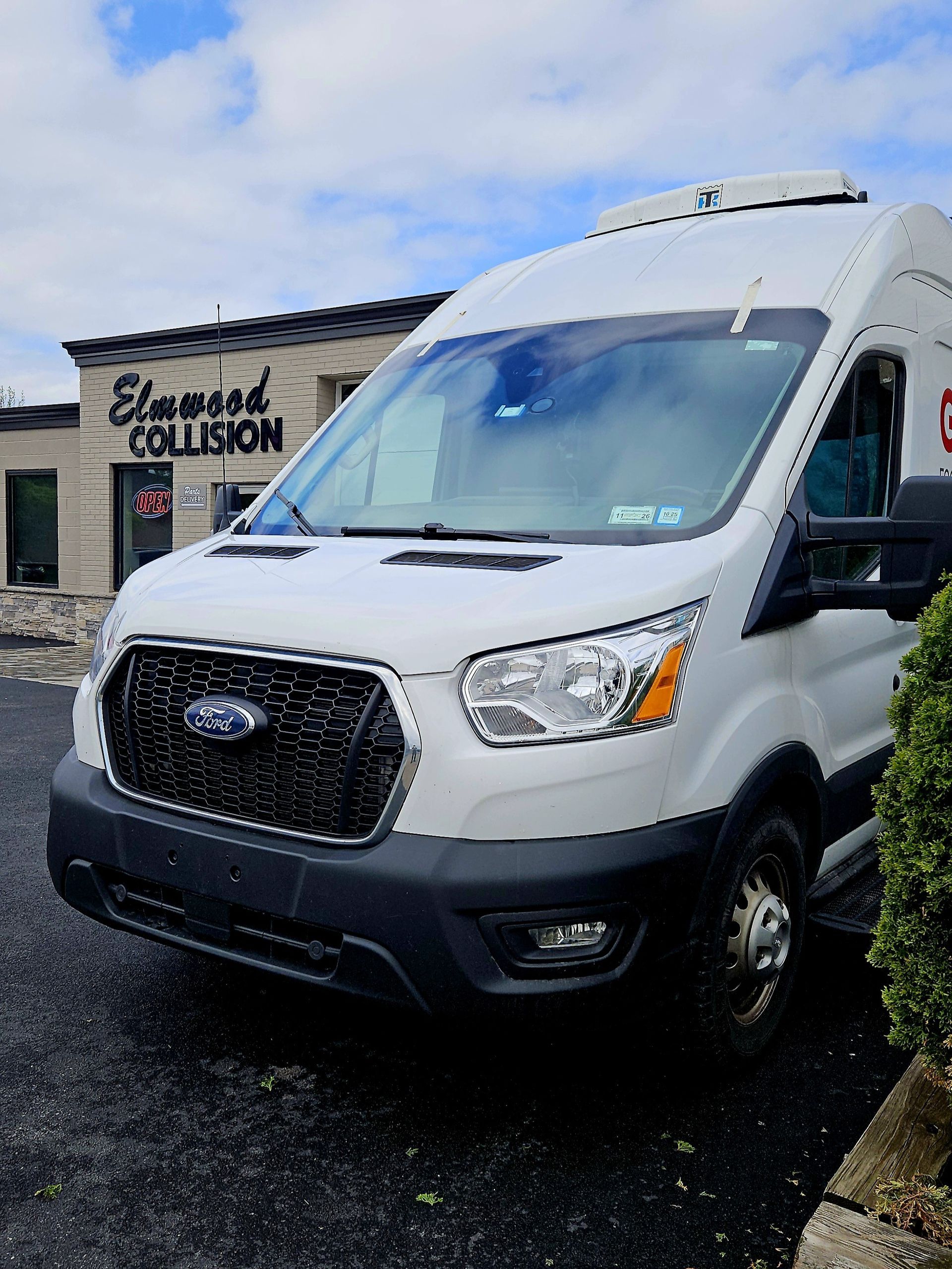A white ford e-transit 350 van is parked in front of elmwood collision.