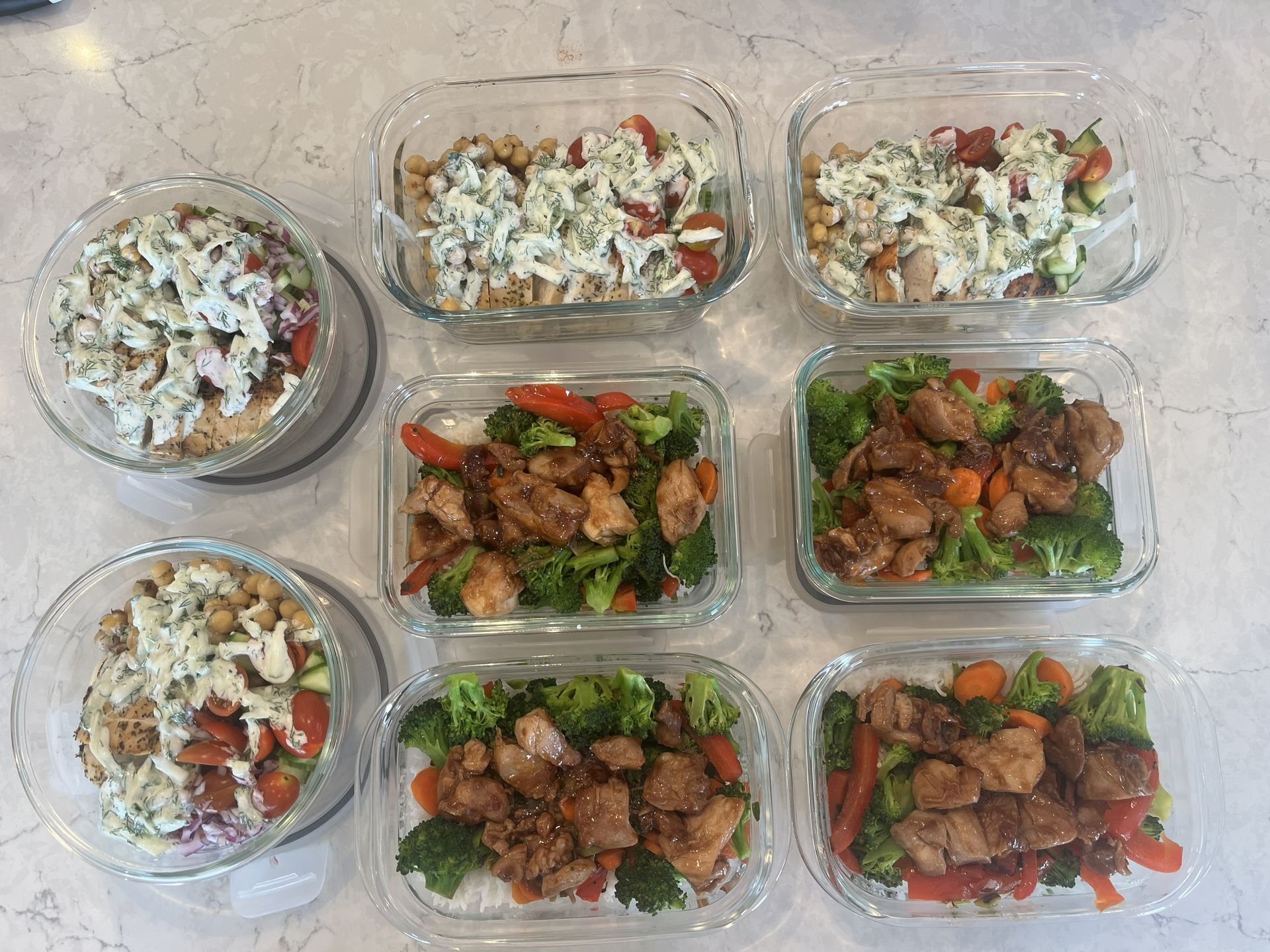 Meal prep containers with mixed chicken, vegetables, and rice on a countertop