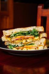 A toasted sandwich on a plate with lettuce, tomato, cheese, and chicken, set on a dark wooden table.