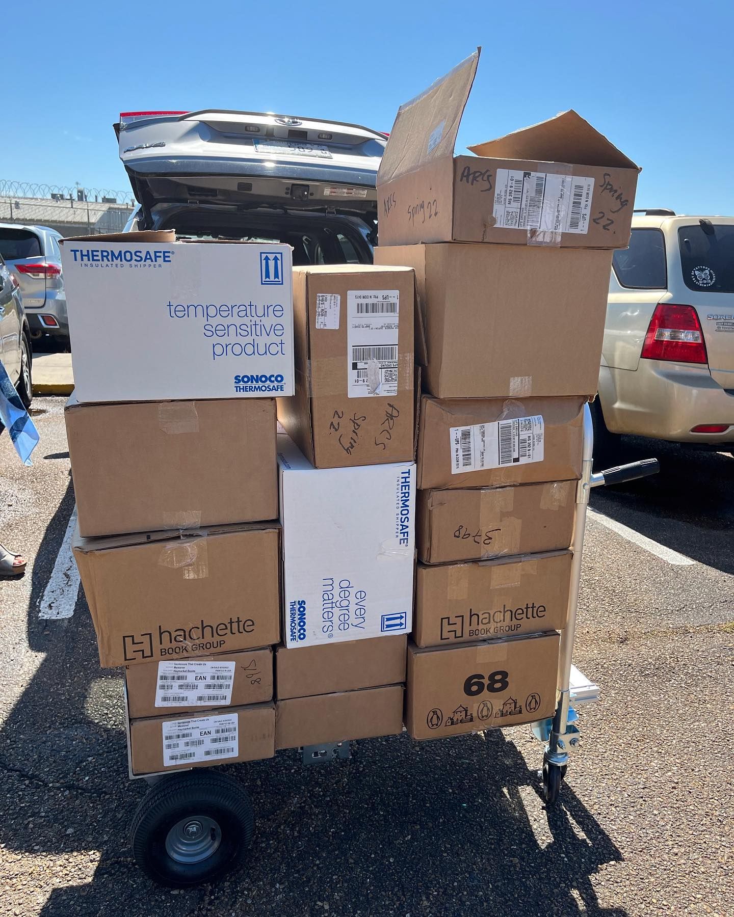 Cart overloaded with cardboard boxes in a parking lot, a boat visible in the background.